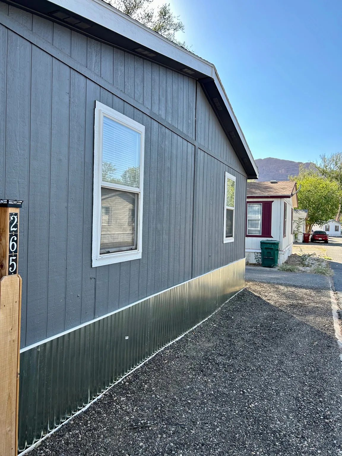 Gray exterior siding featuring white-trimmed windows and corrugated metal skirting
