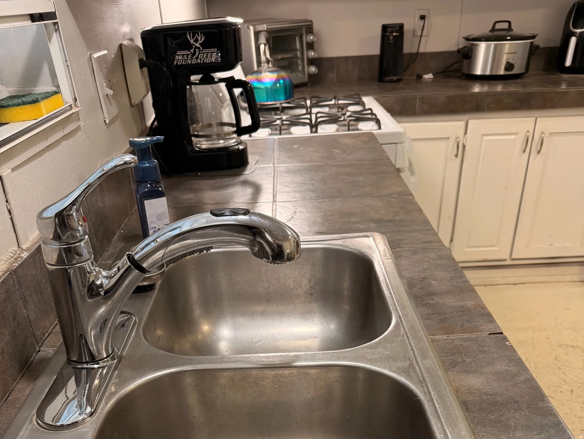 Stainless steel double basin sink with a chrome pull-down faucet, set into a tiled countertop