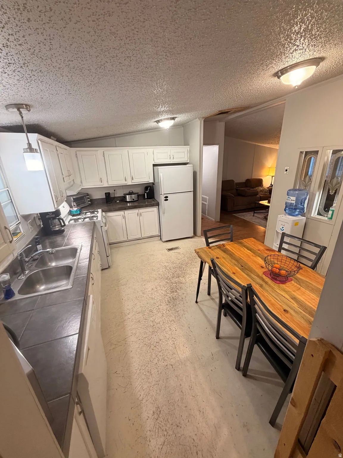 Kitchen featuring white cabinetry, gray countertop, double basin stainless steel sink, and white appliances
