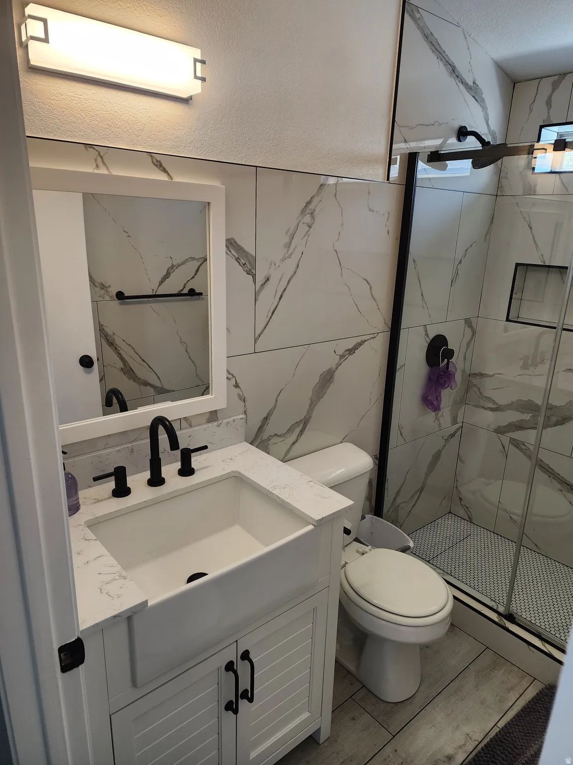 Bathroom featuring a white shaker-style vanity with a farmhouse sink, quartz countertop, and matte black fixtures