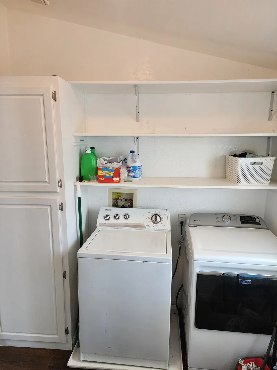Dedicated laundry area featuring white built-in cabinetry, two tiers of open shelving, and wood-finish flooring