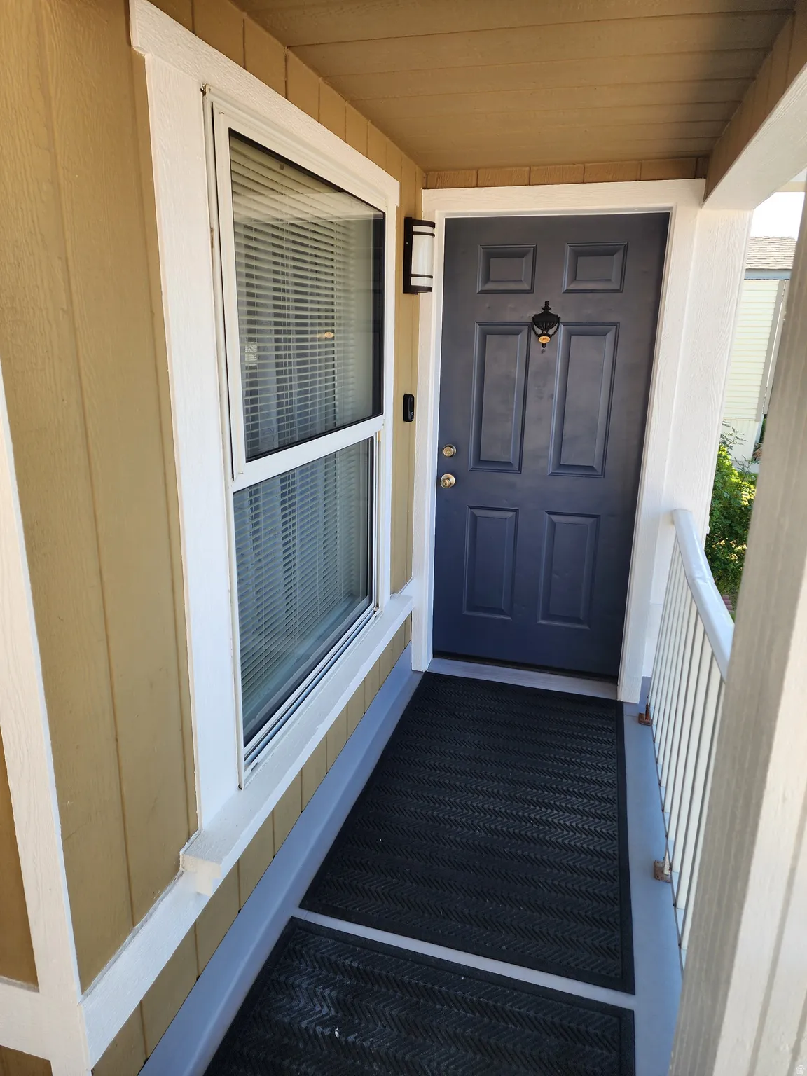 Inviting front porch entrance featuring a paneled door, decorative door knocker, and an exterior wall lantern