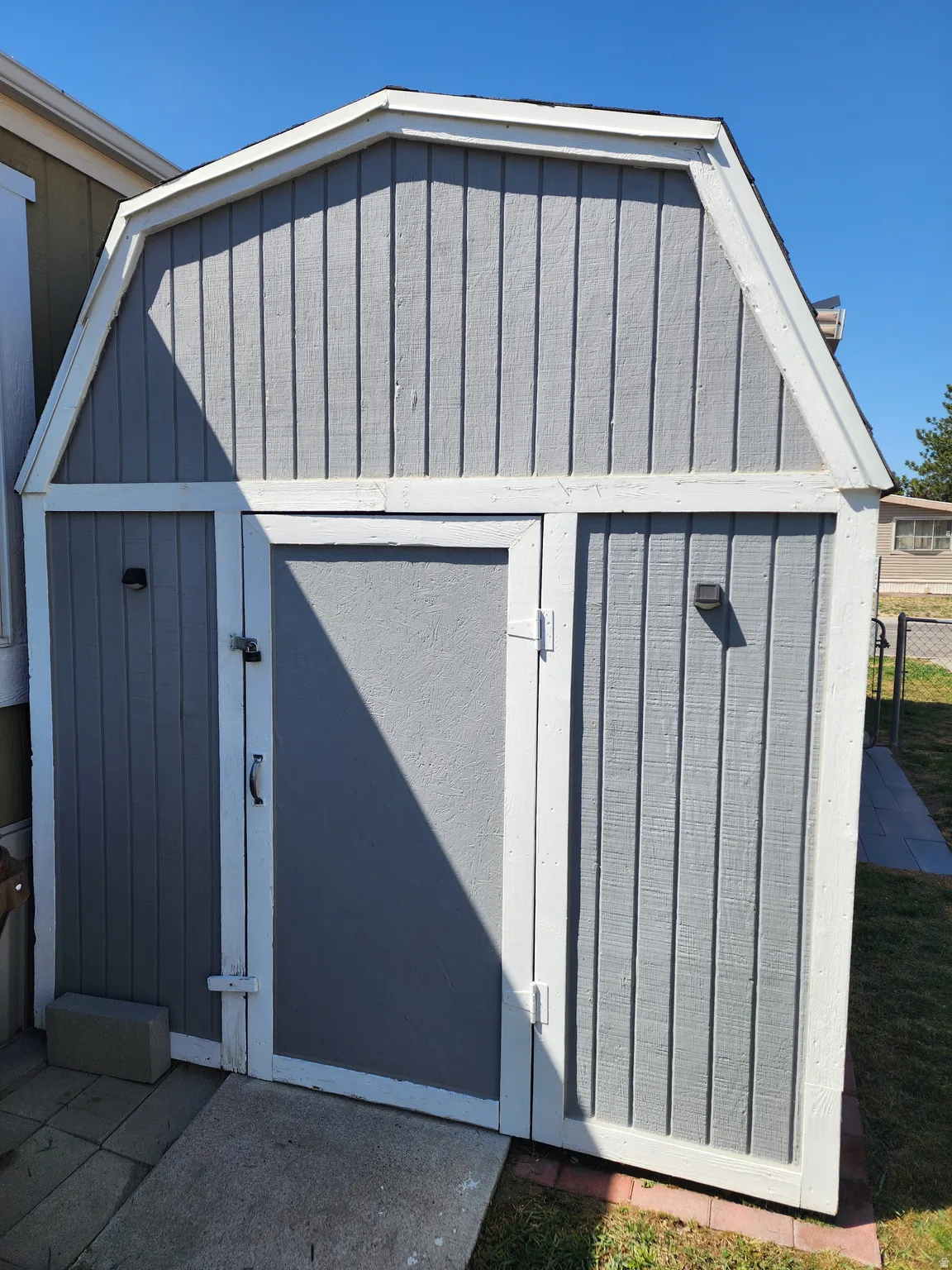 Gray storage shed with white trim and a gambrel roof design