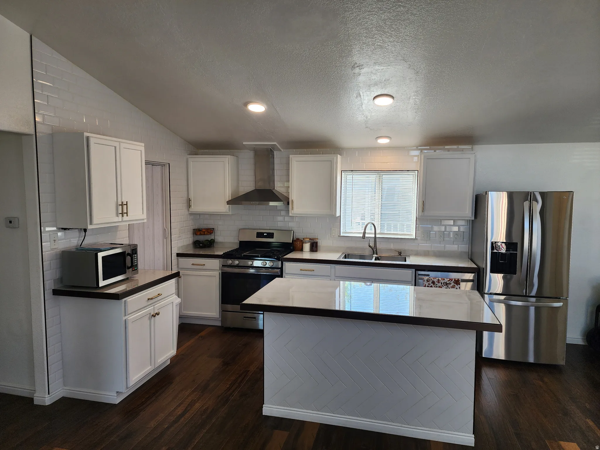 Modern kitchen featuring white cabinetry, dark countertops, wood-finish flooring, a herringbone-patterned island, and stainless steel appliances