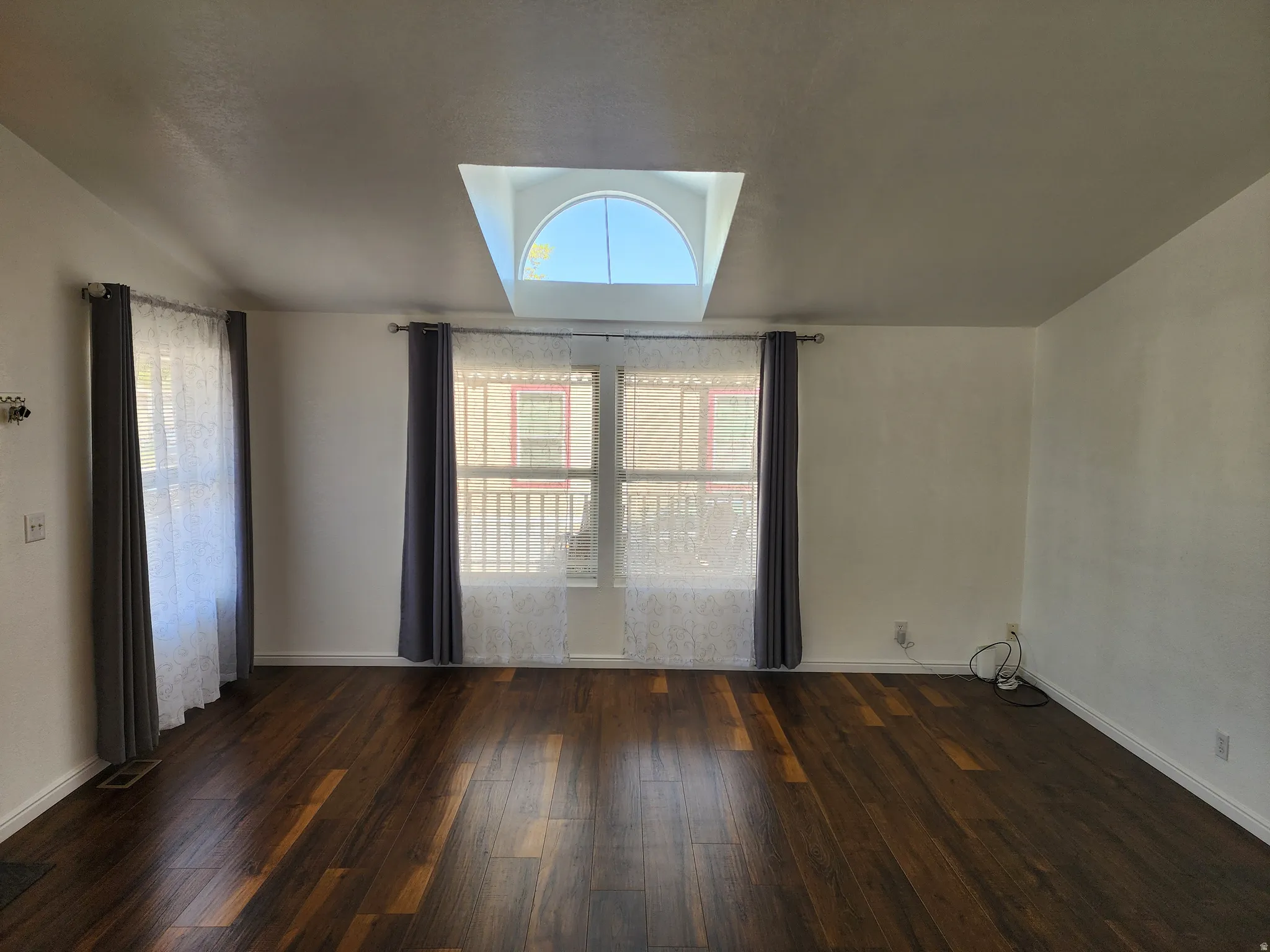Expansive living area featuring rich wood-finish flooring, a prominent arched skylight, and multiple windows