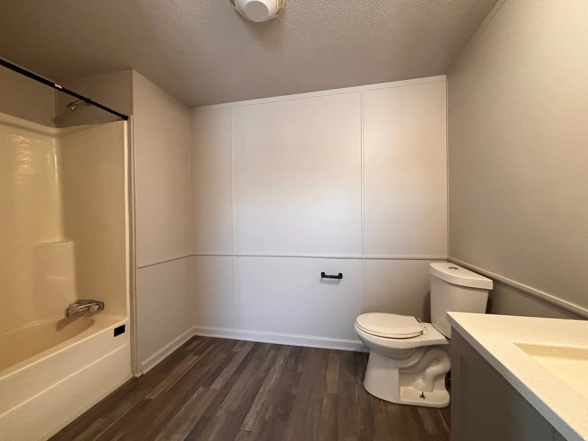 Bathroom featuring a single vanity with an integrated sink, a toilet, a shower-tub combination with a chrome faucet, and wood-finish flooring