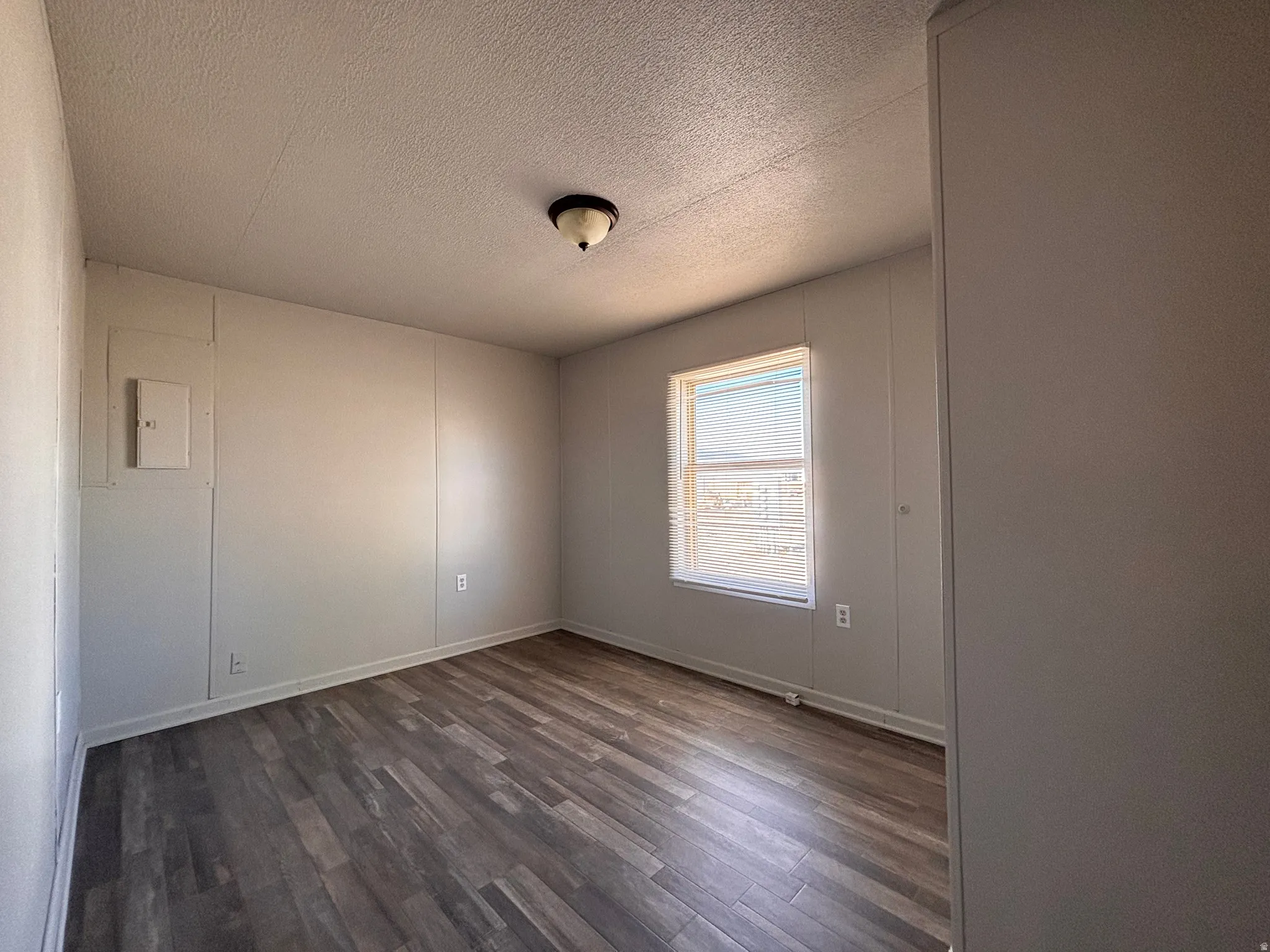 Interior room featuring wood-finish flooring, light gray wall paneling, and a single window with blinds