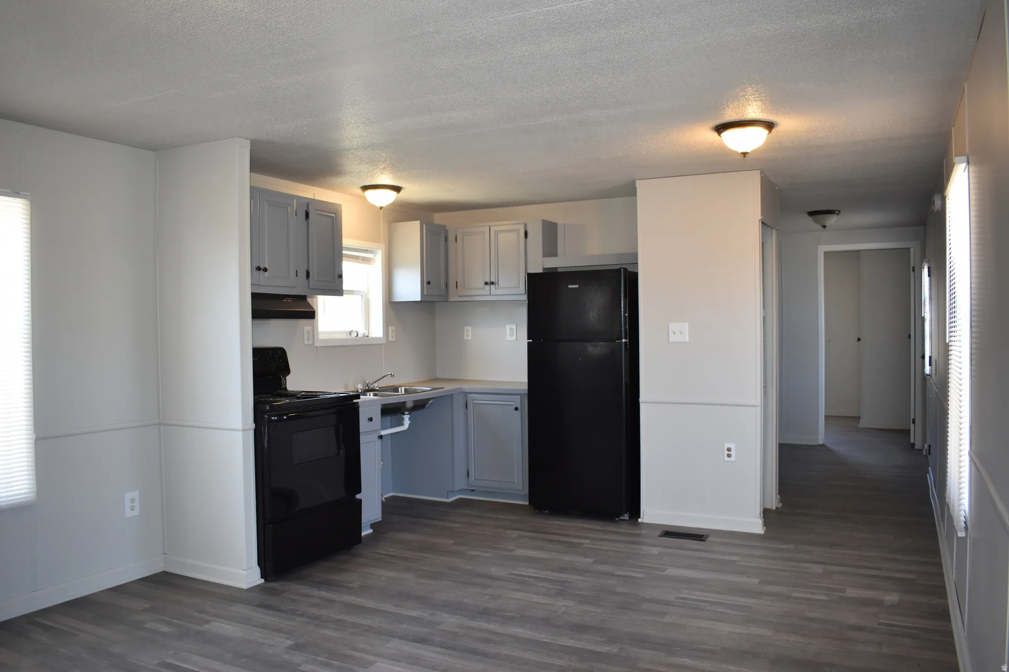 Open-concept living space with wood-finish flooring, a kitchen featuring gray cabinetry, black appliances, and white countertops, and recessed lighting fixtures