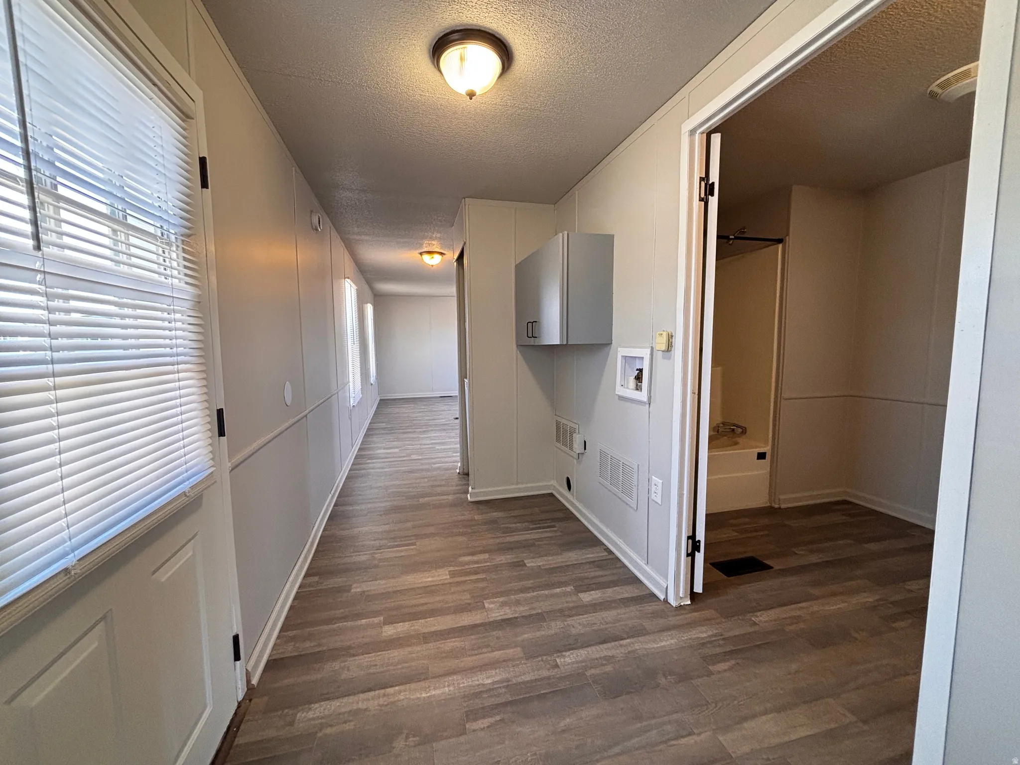 Hallway featuring wood-finish flooring, white panel walls, and multiple windows with blinds