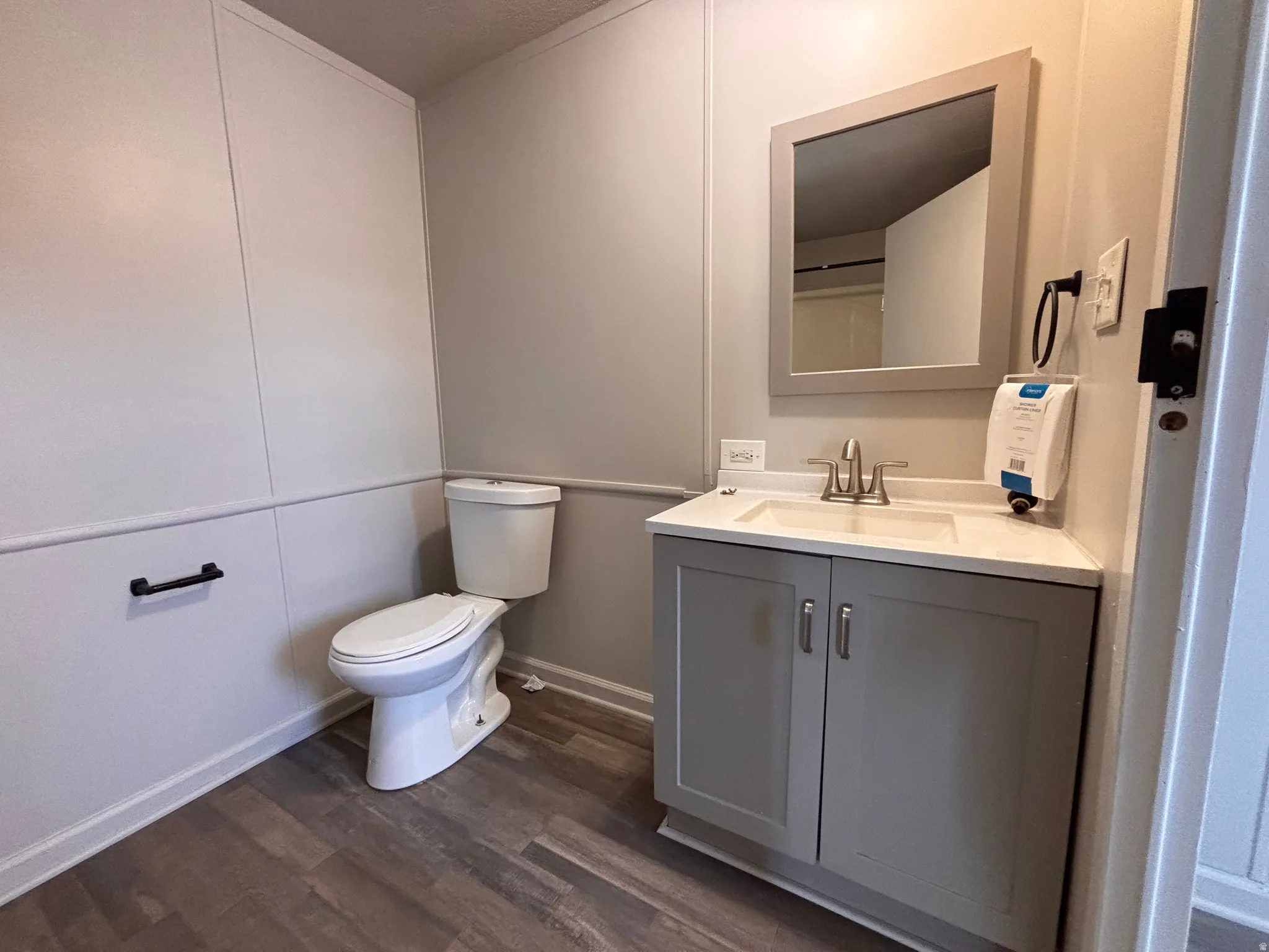 Bathroom featuring wood-finish flooring, a white toilet, and wainscoting