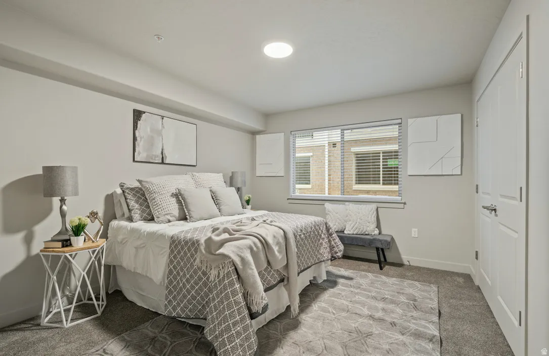 Bedroom featuring plush carpeting, a large window with horizontal blinds, and a built-in closet with panel doors