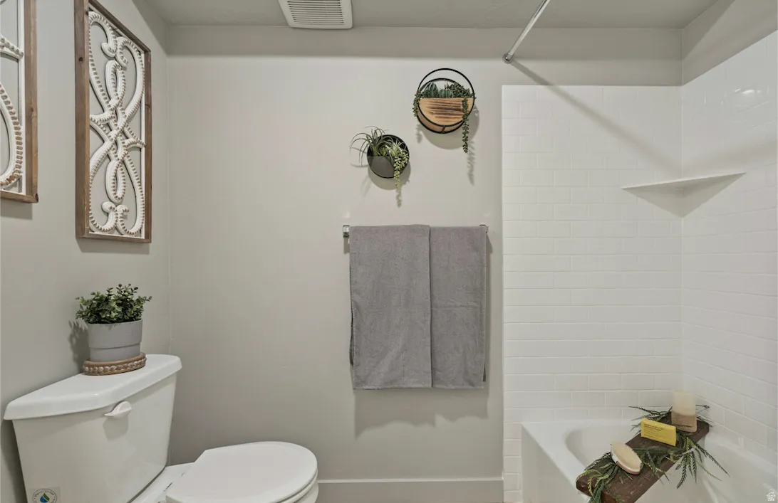 Modern bathroom featuring a white porcelain toilet, a white subway tile tub surround with an integrated corner shelf, and a built-in towel bar