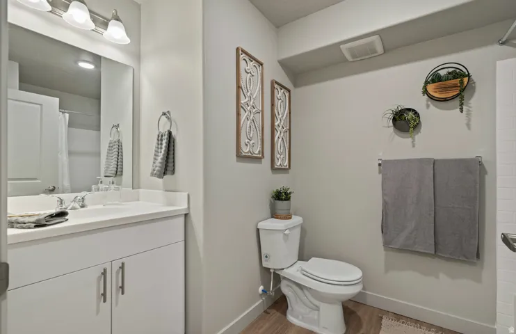 Bathroom featuring a vanity with a white countertop and base cabinetry, a wall-mounted mirror, brushed nickel light fixture, wood-finish flooring, and a white toilet