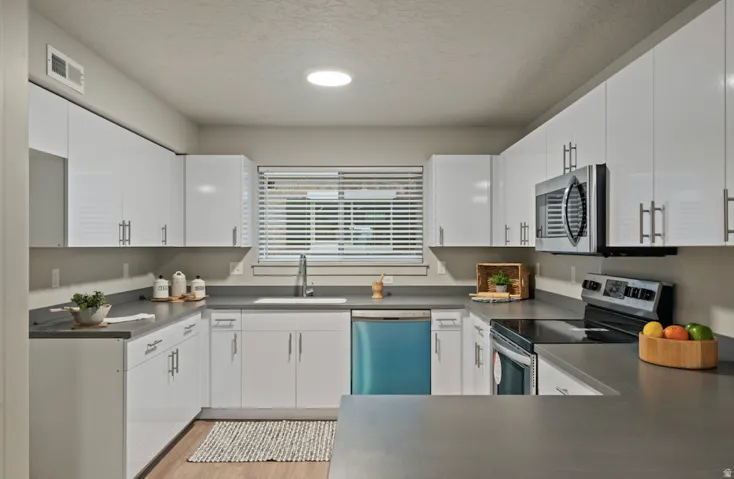 U-shaped kitchen featuring white cabinetry, gray countertops, and stainless steel appliances