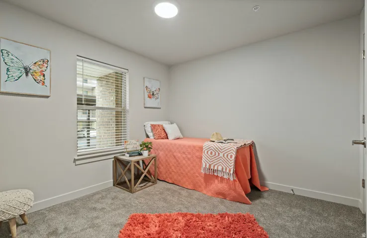 Recessed ceiling lighting illuminates a room featuring a window with horizontal blinds, gray wall paint, and gray carpet flooring