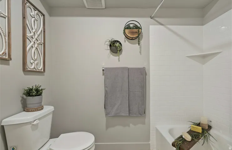 Modern bathroom featuring a white porcelain toilet, a white subway tile tub surround with an integrated corner shelf, and a built-in towel bar