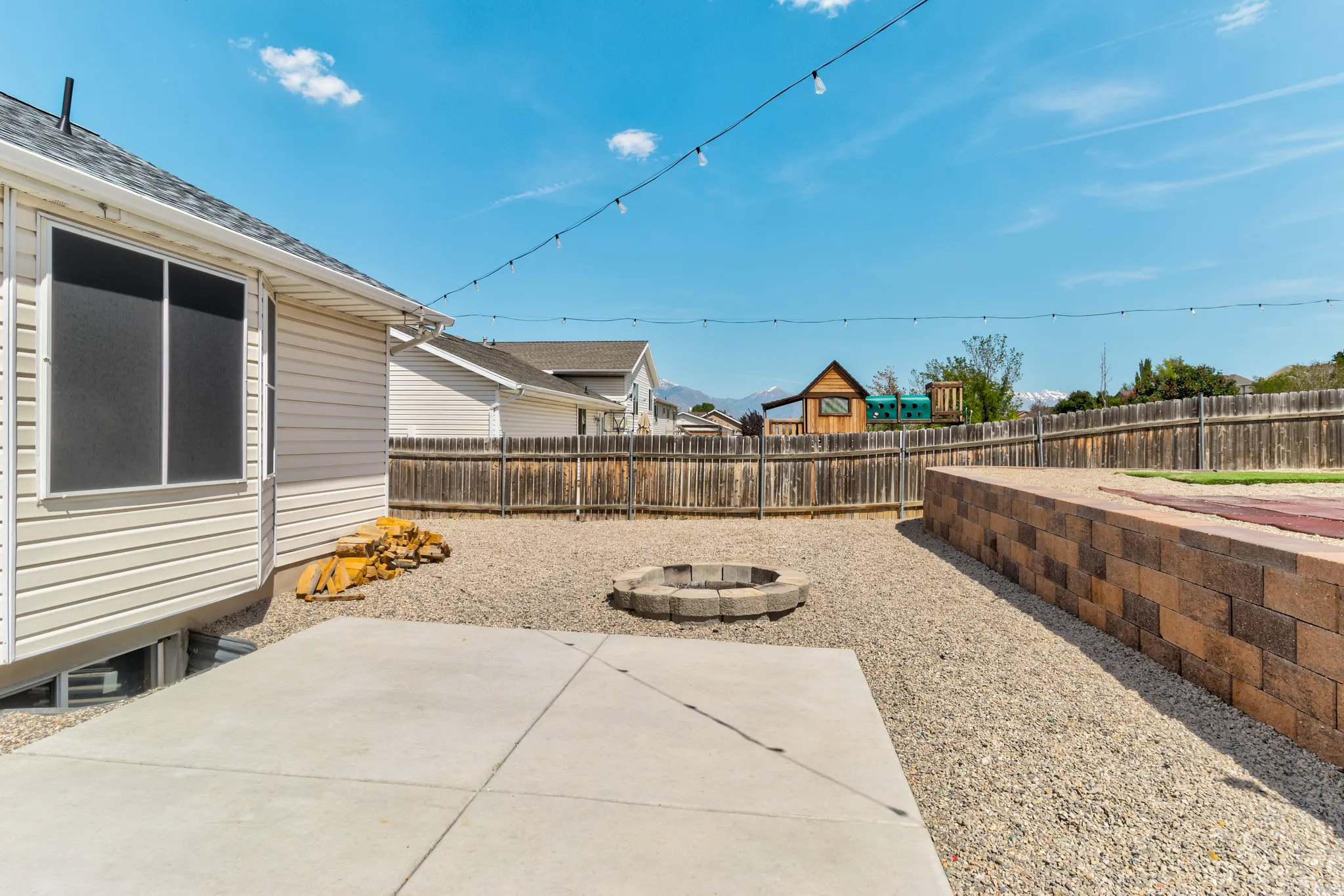 Gravel backyard featuring a concrete patio, built-in fire pit, and a retaining wall