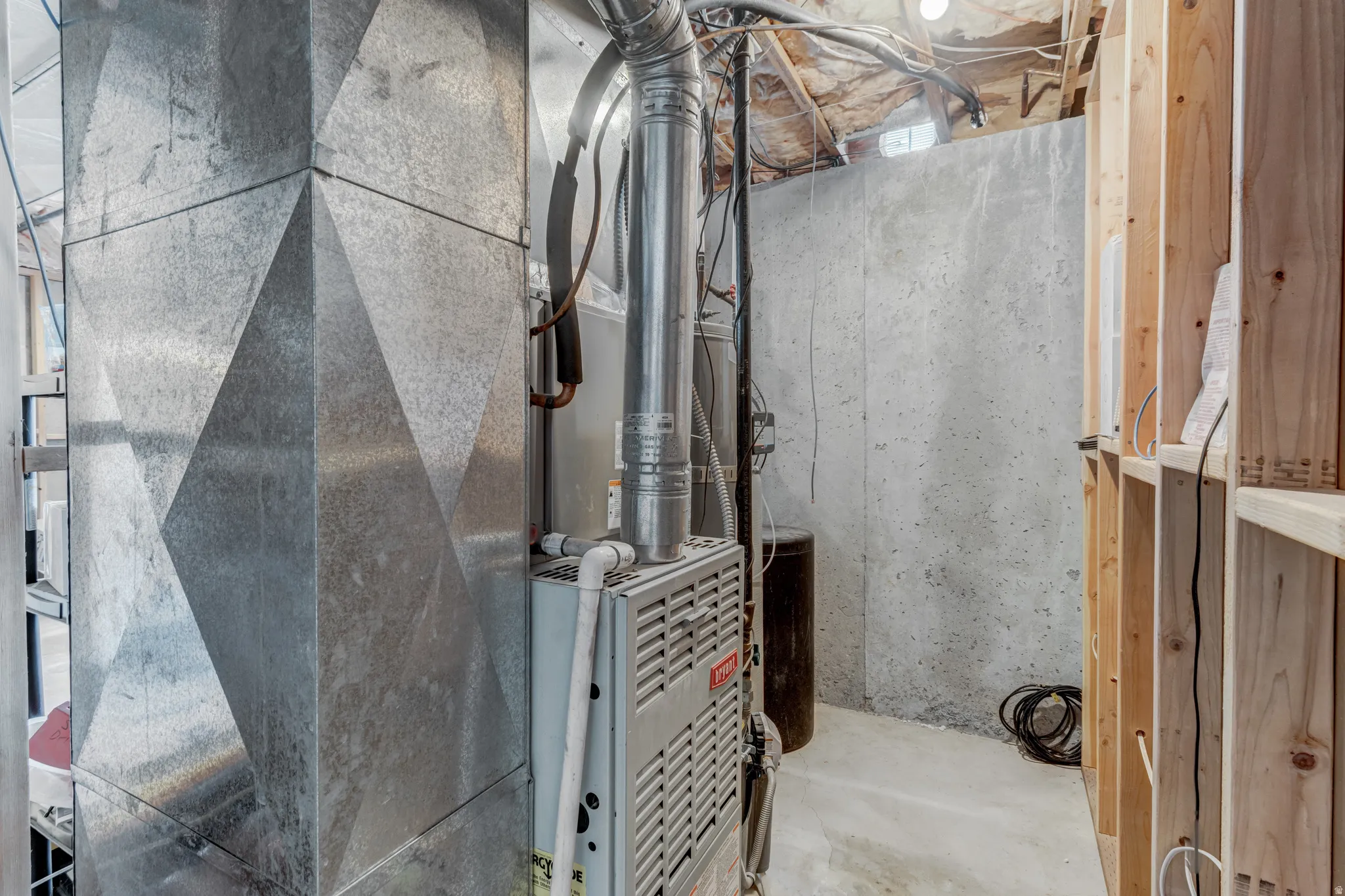 Galvanized HVAC ductwork, furnace unit, concrete foundation wall, exposed ceiling joists, and wood stud framing