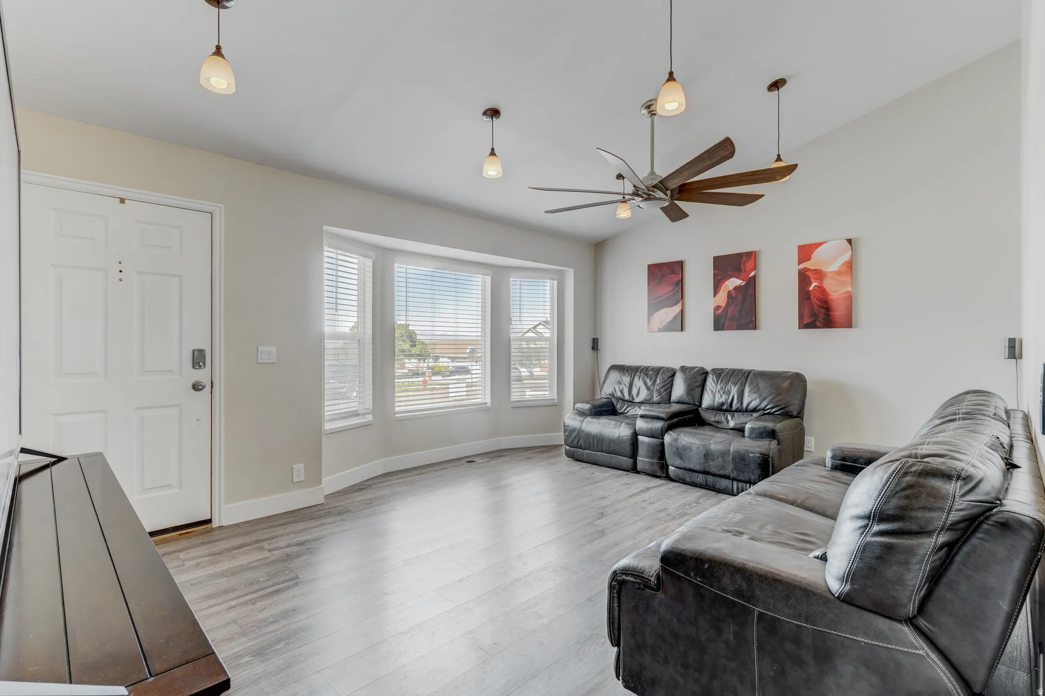 Spacious living area featuring wood-finish flooring, a contemporary ceiling fan, and multiple windows with blinds