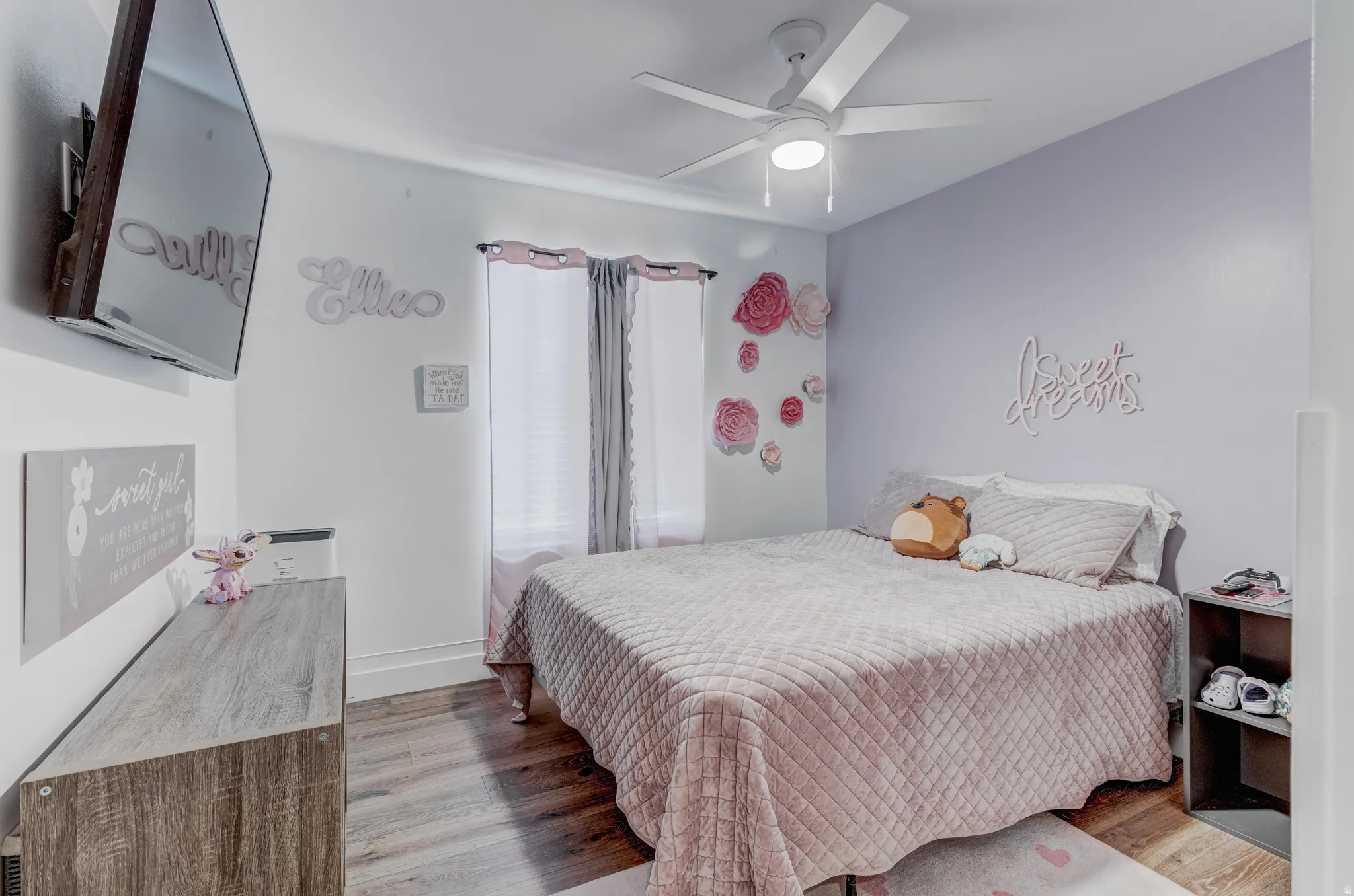 Bedroom featuring wood-finish flooring, a ceiling fan with integrated lighting, and a window with curtains