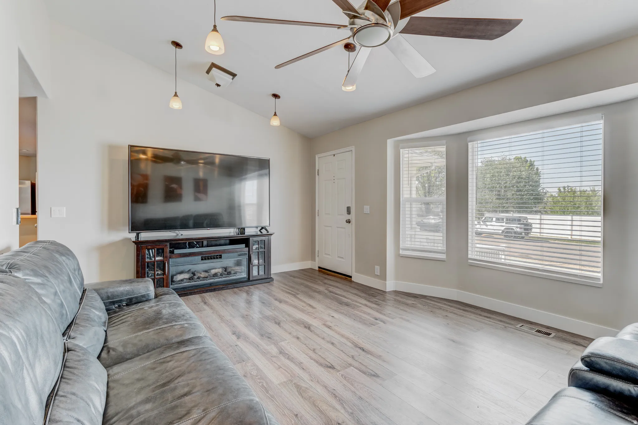 Living area featuring vaulted ceilings, wood-finish flooring, a contemporary ceiling fan, and multiple windows
