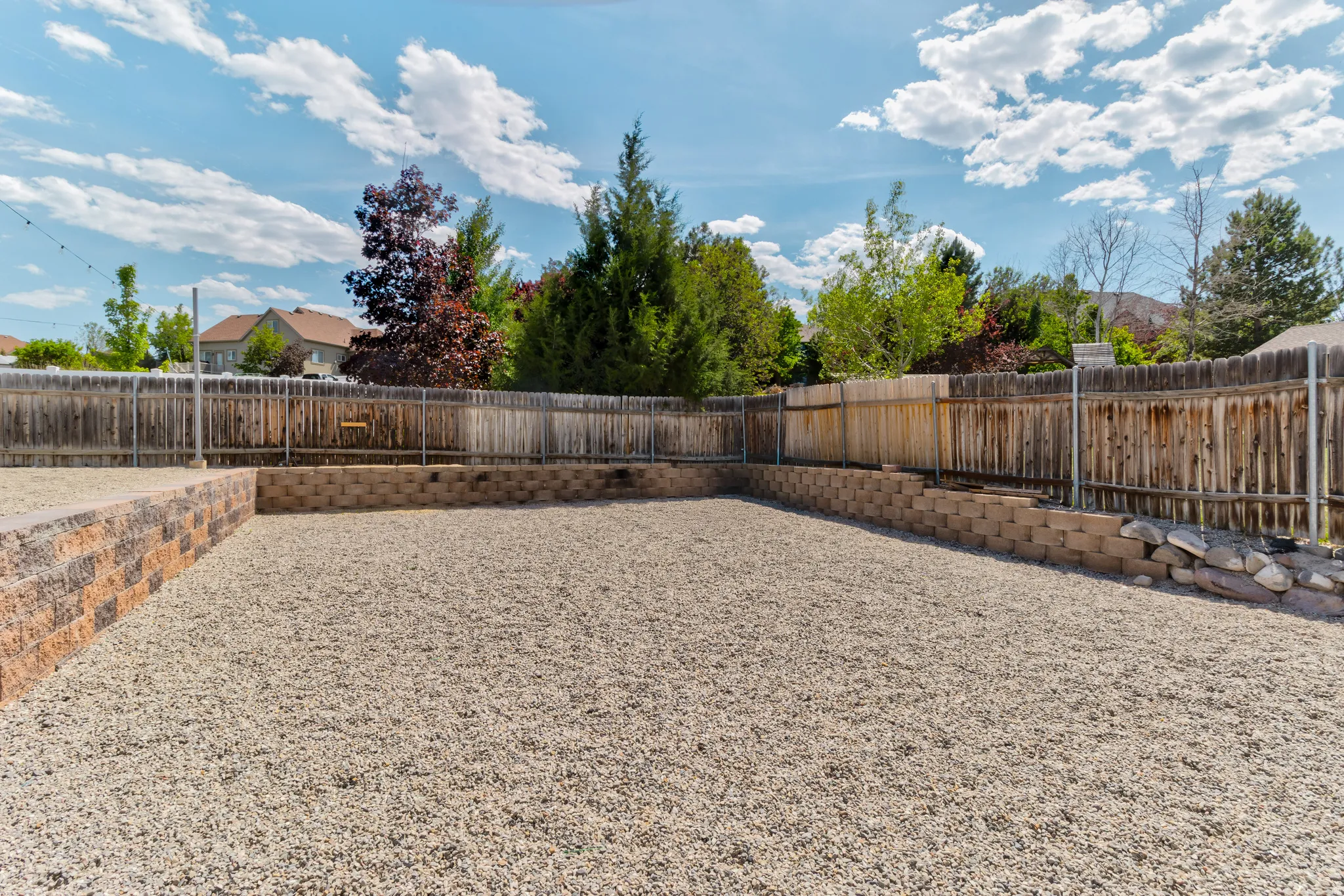 Expansive gravel yard featuring a wood privacy fence, terraced retaining walls, and surrounding mature trees