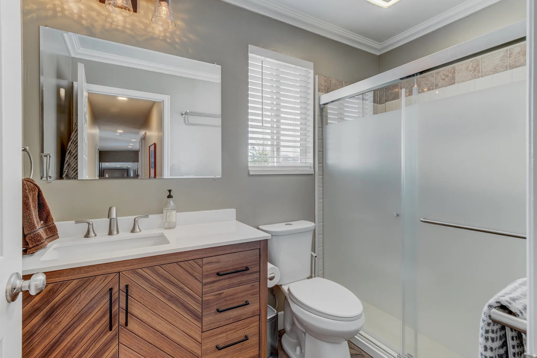 Bathroom featuring a wood-finish vanity with a white countertop, an integrated rectangular sink, and a brushed nickel faucet