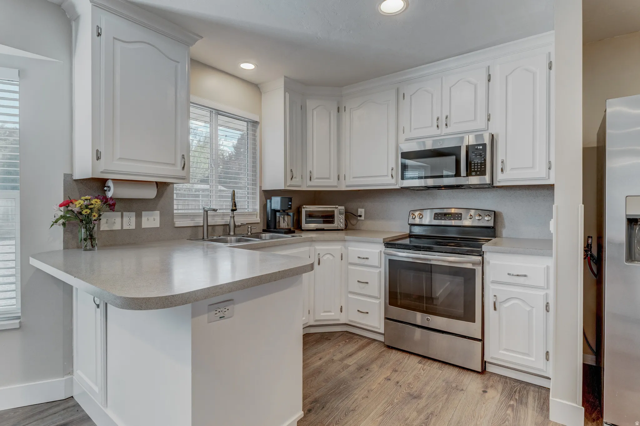 Kitchen featuring white cabinetry with brushed nickel hardware, light-toned countertops, and wood-finish flooring
