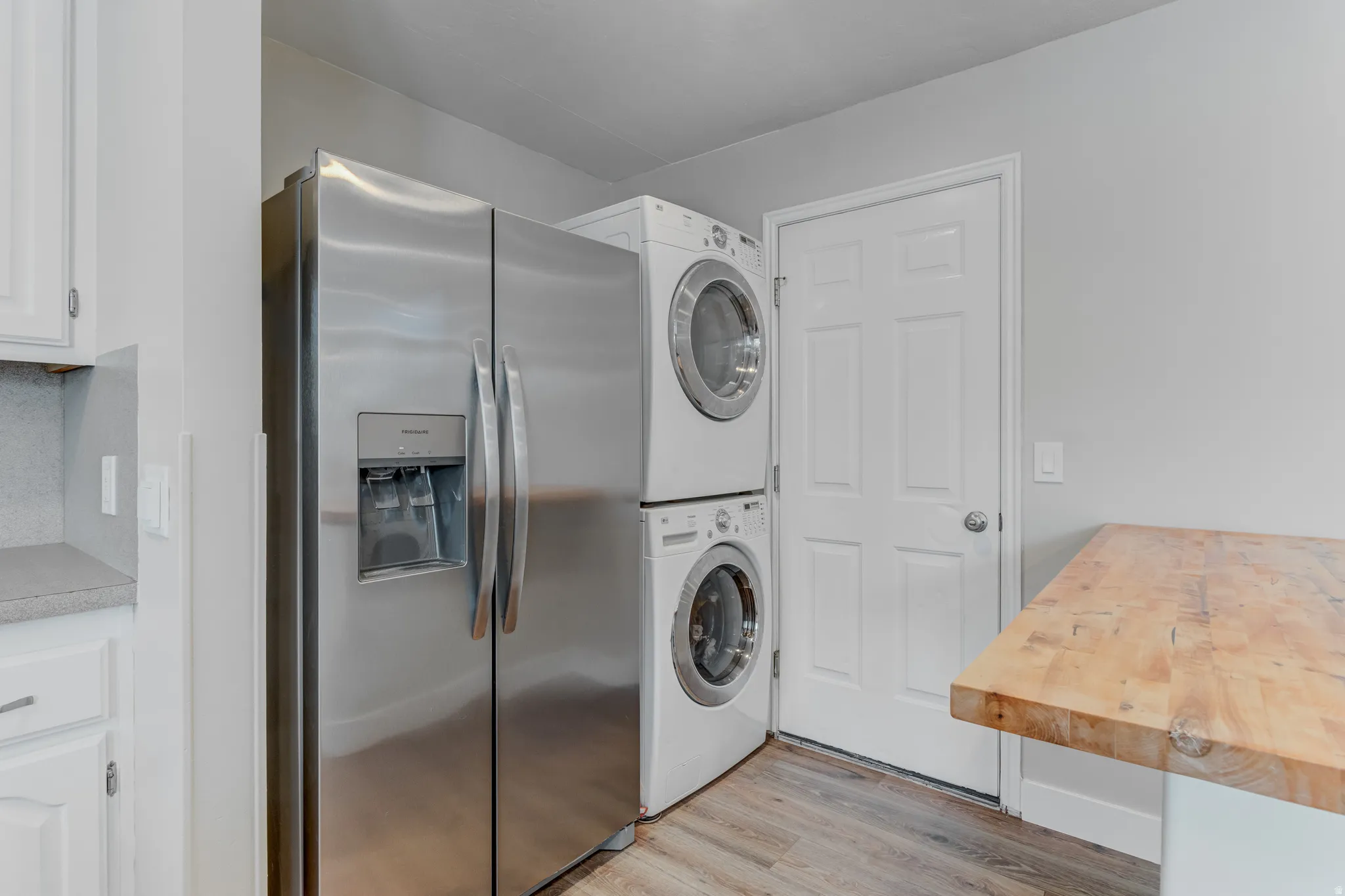 Stainless steel refrigerator with a water and ice dispenser, stacked washer and dryer, and a wooden butcher block countertop