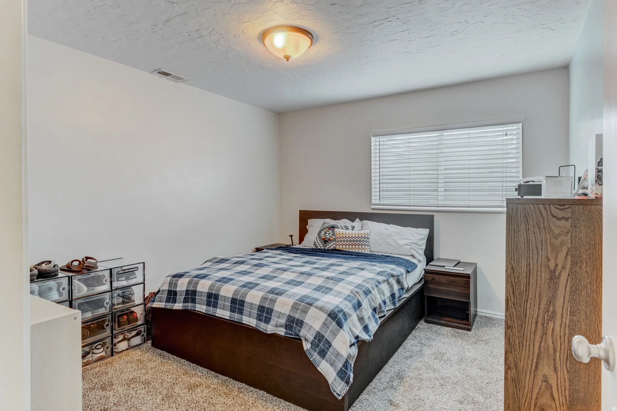 Bedroom featuring neutral wall paint, textured carpeting, a single window with blinds, and a flush-mount ceiling light fixture