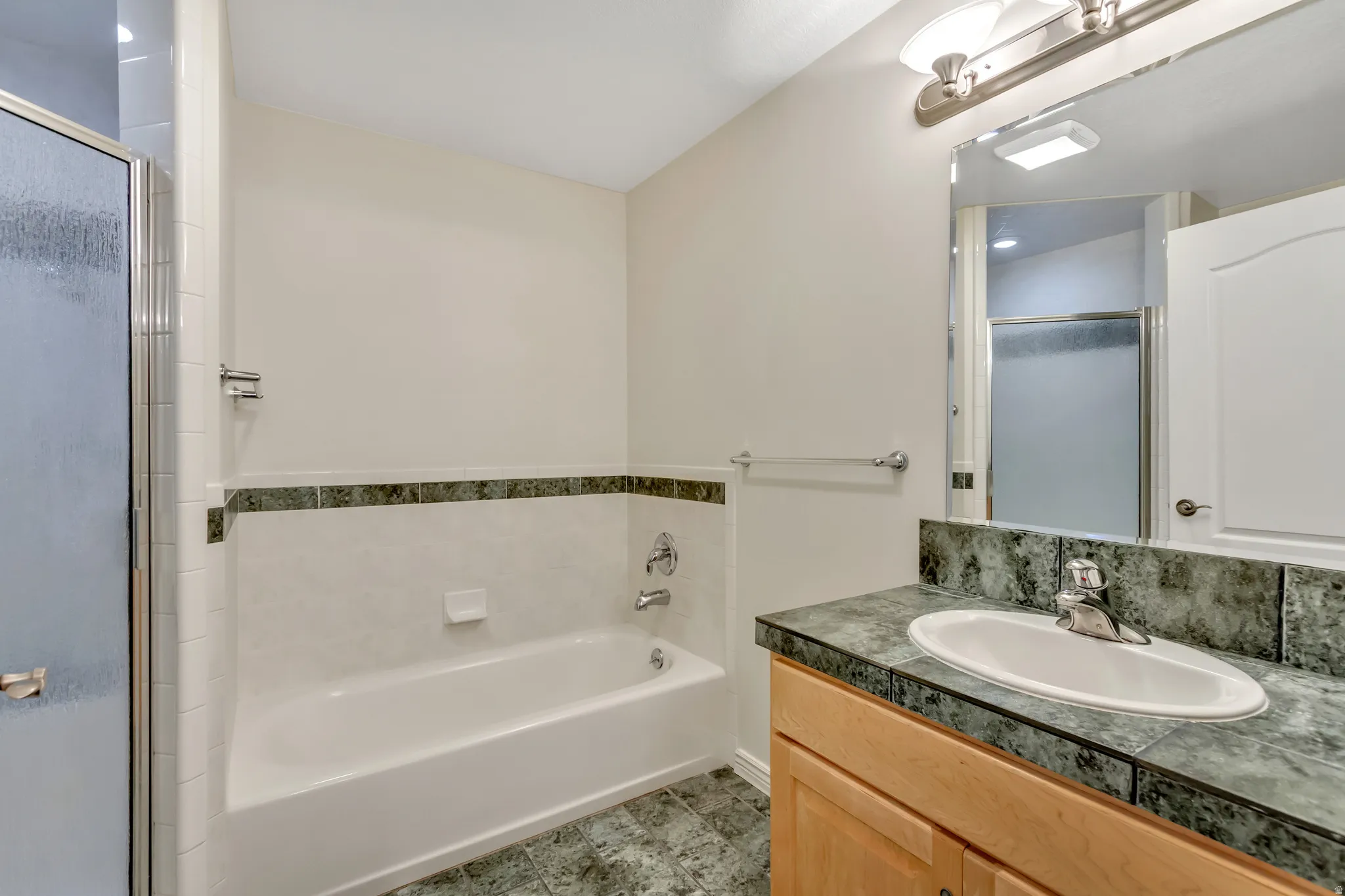 Bathroom featuring a white bathtub, a glass-enclosed shower, a vanity with a drop-in sink, and a mirrored medicine cabinet