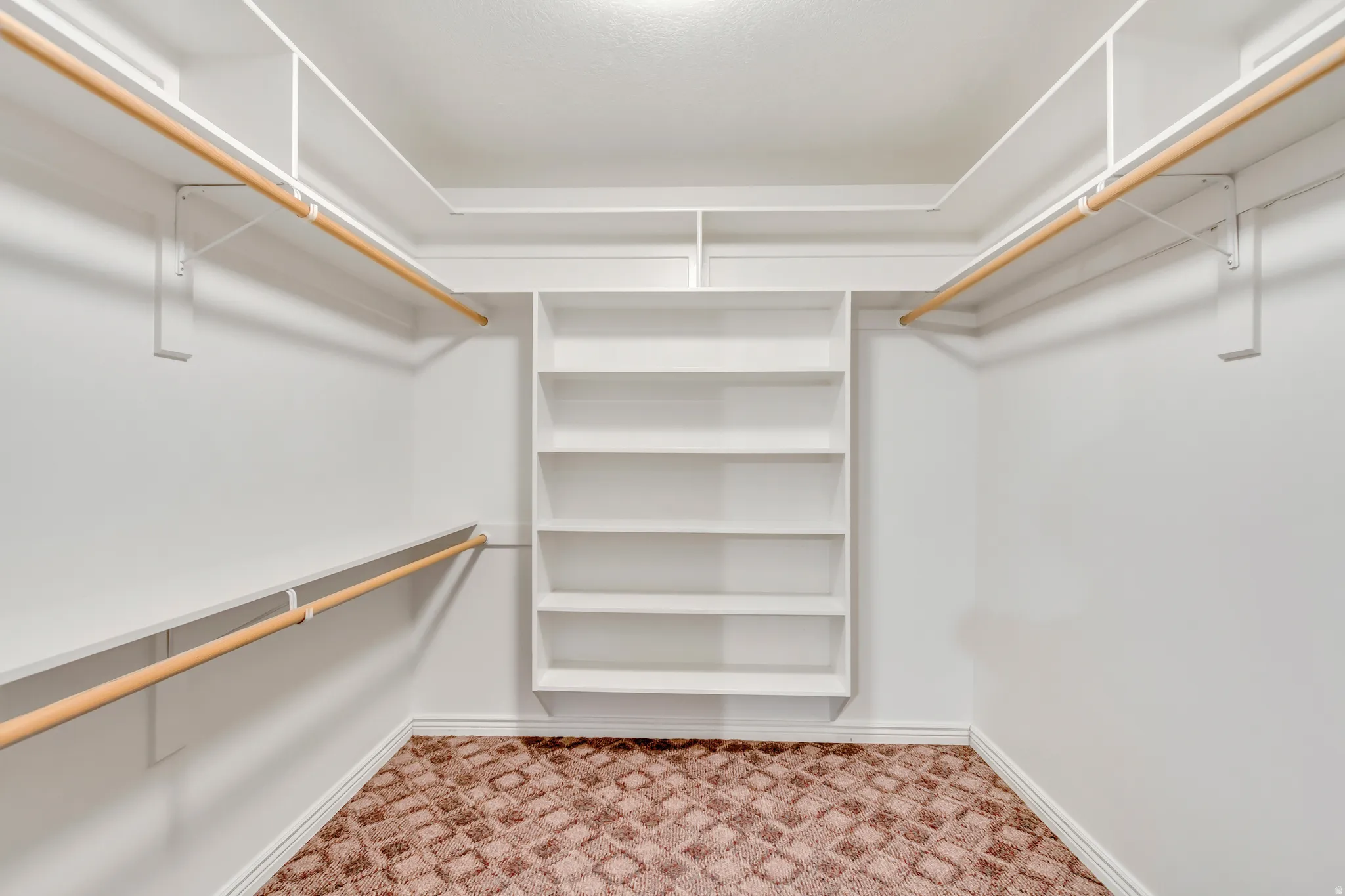 Walk-in closet featuring built-in shelving, multiple hanging rods, white walls, and patterned carpeting