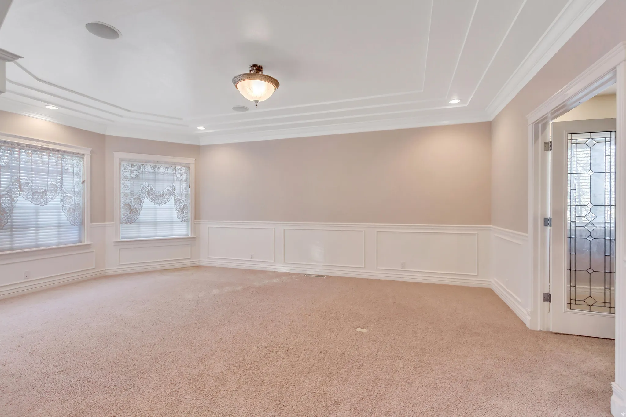 Recessed lighting and a decorative ceiling fixture illuminate this room, featuring a tray ceiling and crown molding