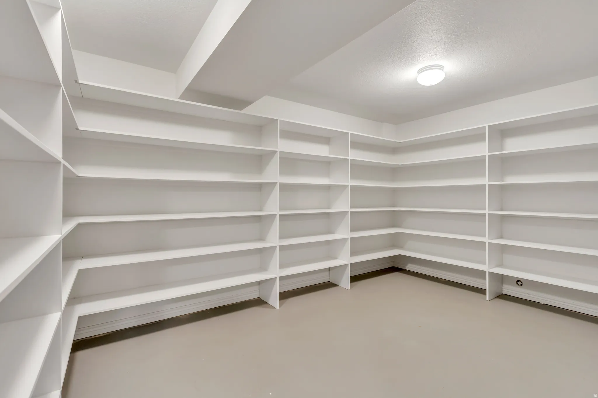 Spacious storage room featuring extensive built-in white shelving, recessed lighting, and neutral flooring