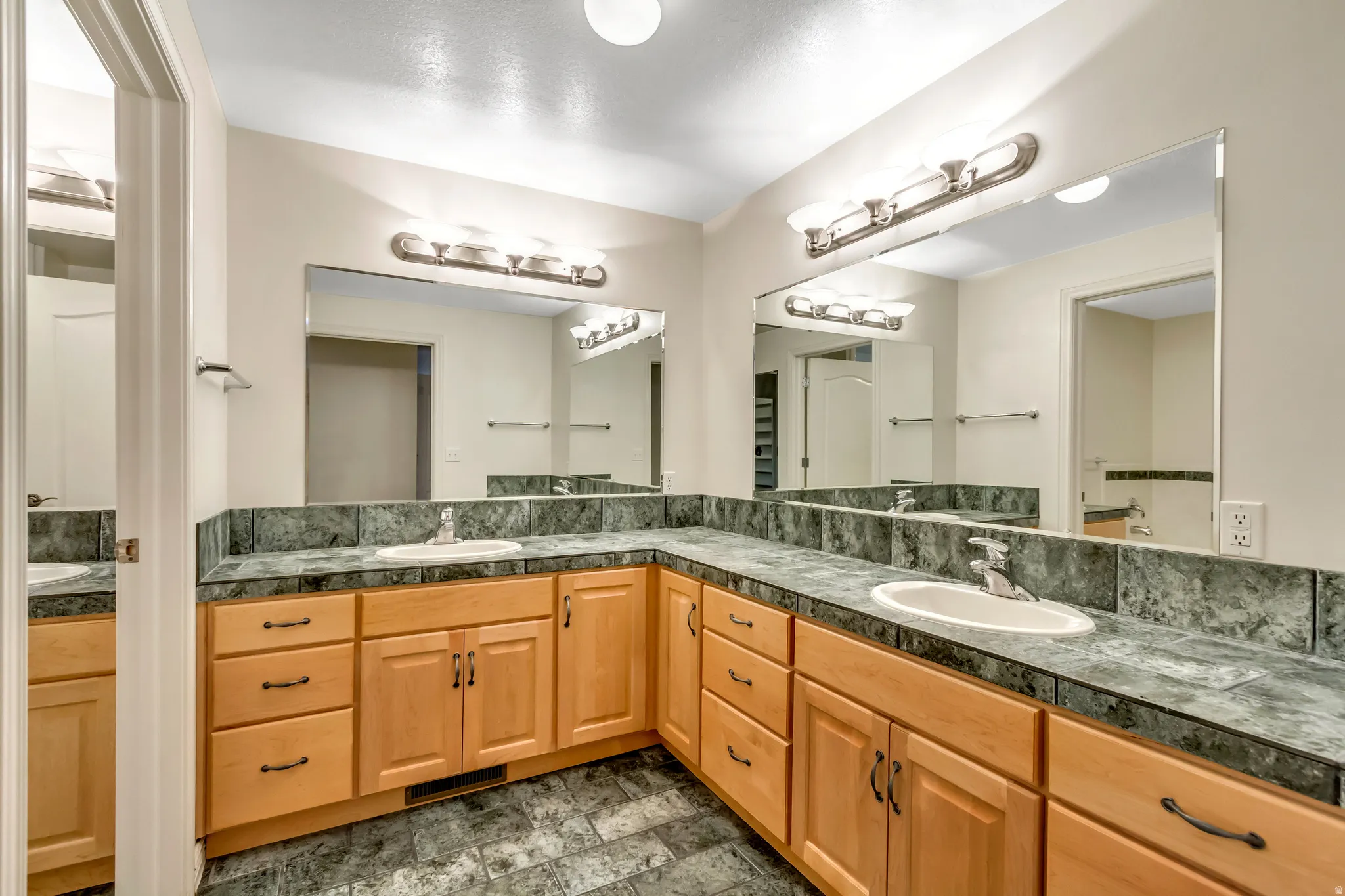 Dual vanity with light wood cabinetry, green patterned countertops, and integrated sinks