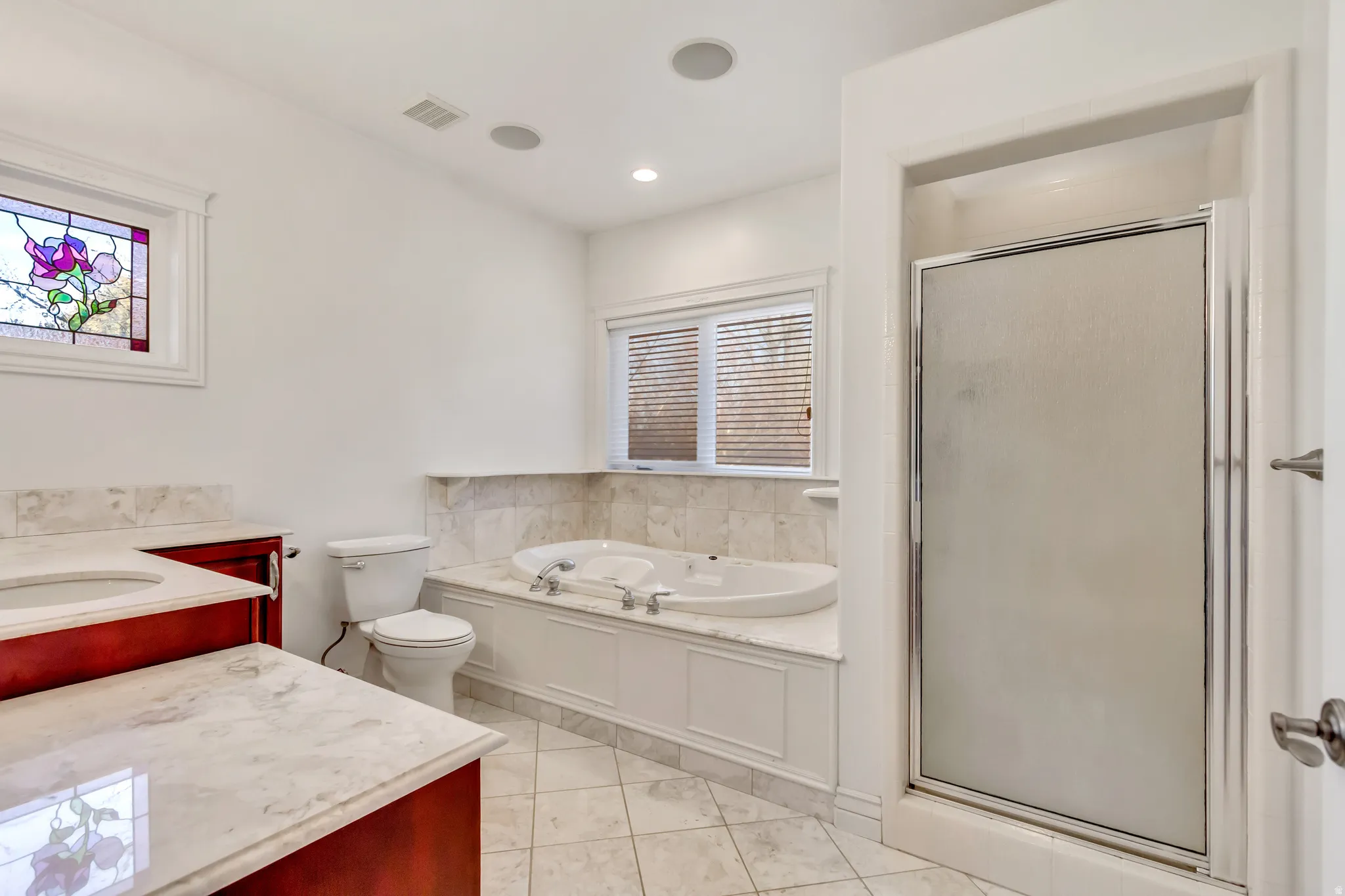 Bathroom featuring a jetted soaking tub with a tiled surround, a separate shower with a frosted glass door, and dual vanity sinks with stone countertops