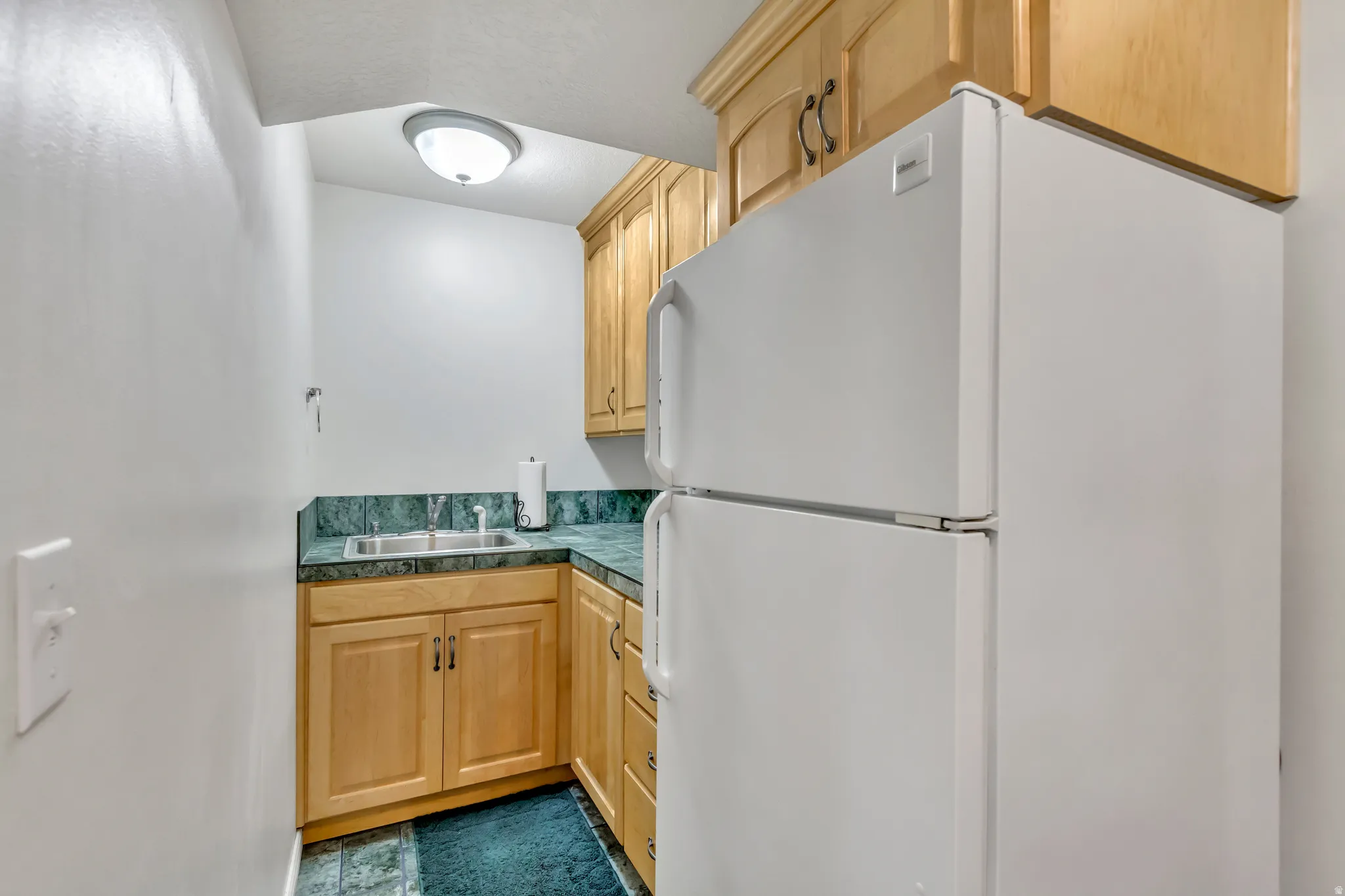 Compact kitchen area featuring a built-in stainless steel sink, wood-finish cabinetry, and green stone-look countertops