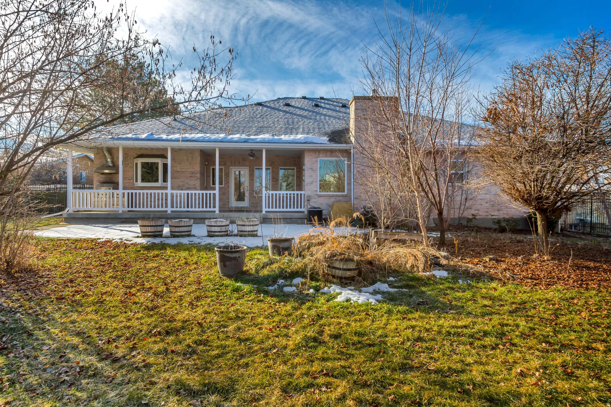 Rear exterior featuring a covered patio with white railings, a bay window, and a brick facade