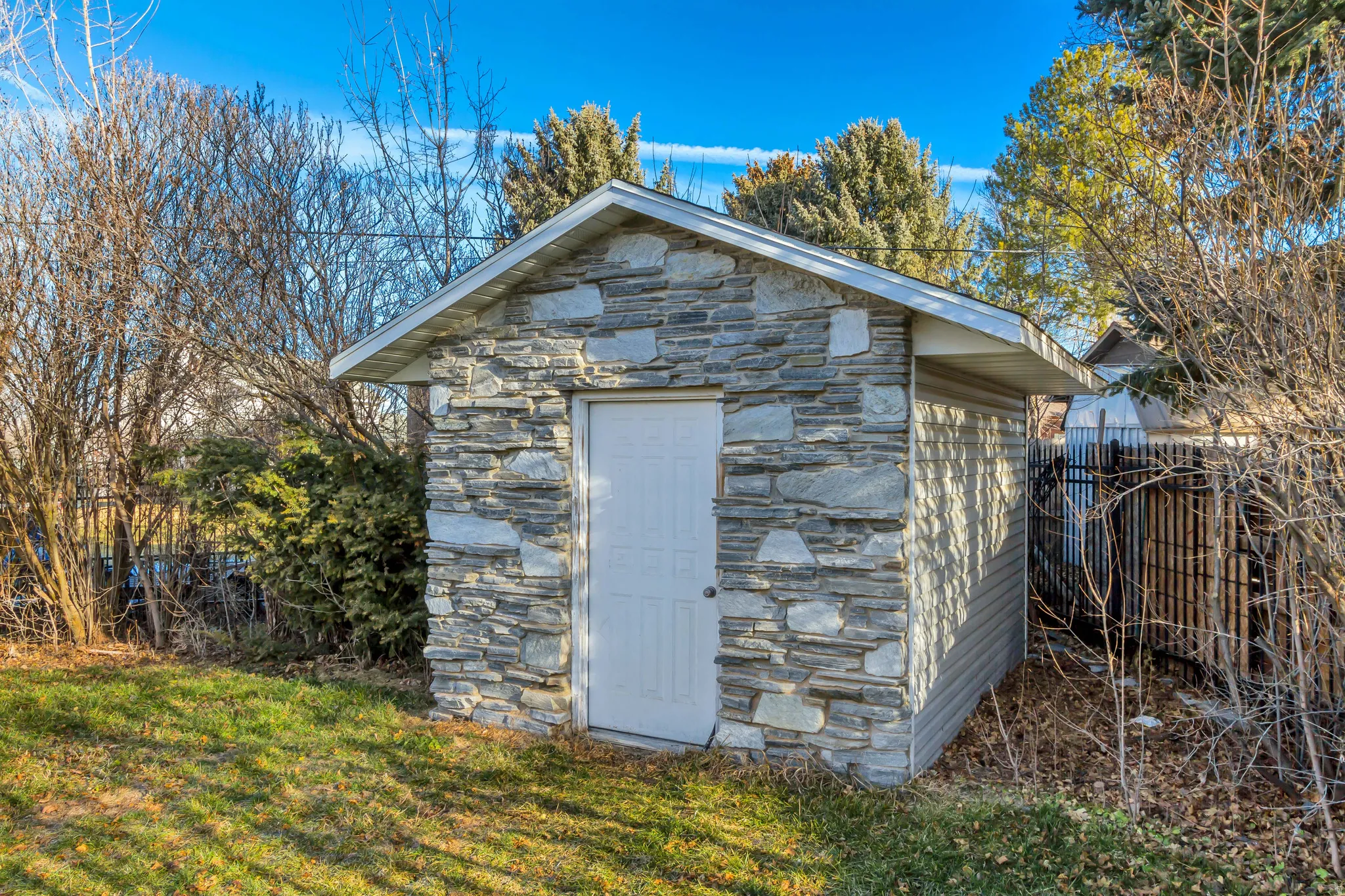 Storage shed featuring a stone veneer facade, white entry door, and vinyl siding