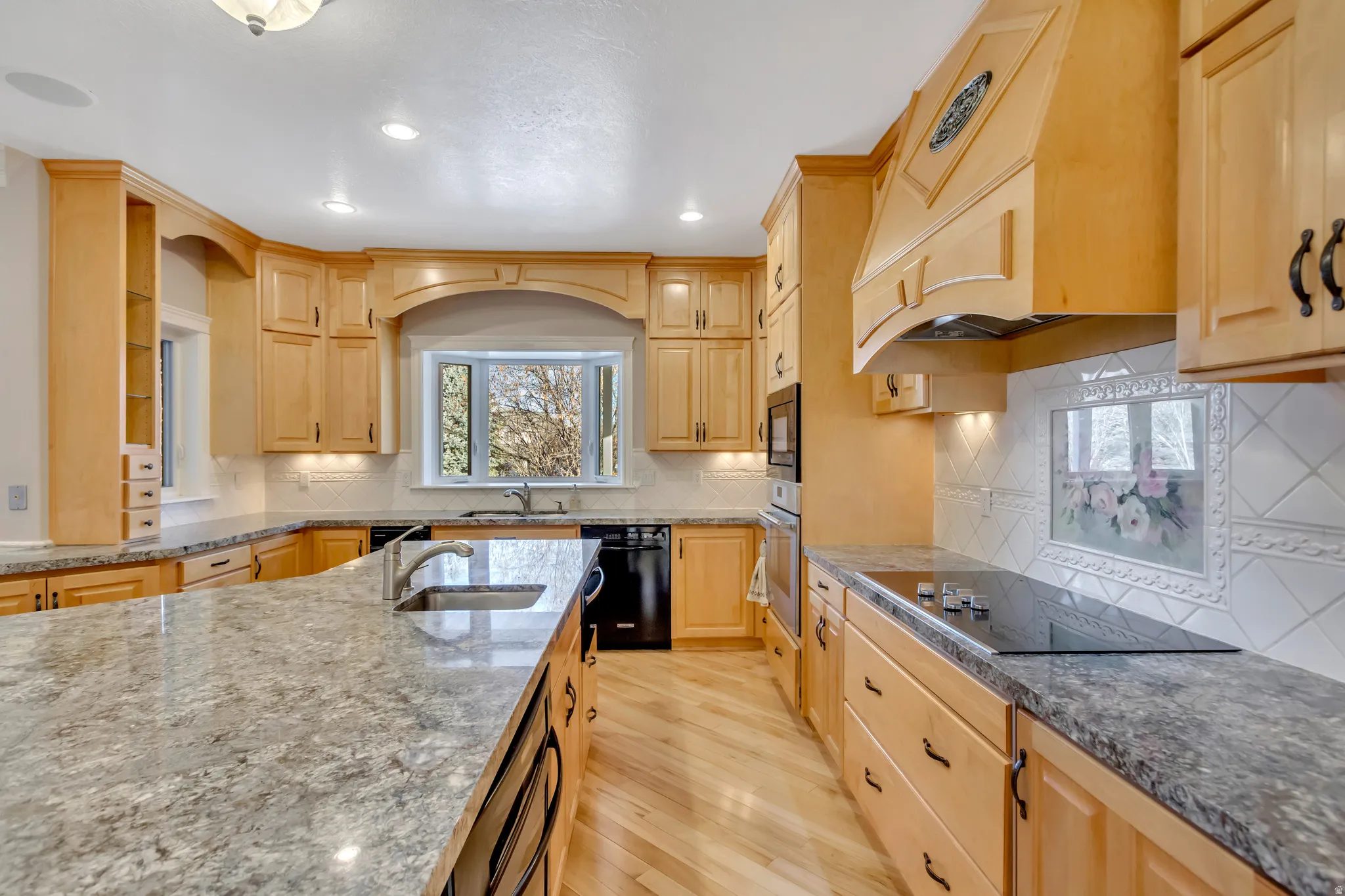 Kitchen featuring light wood cabinetry, stone countertops, integrated cooktop, built-in oven, and wood-finish flooring