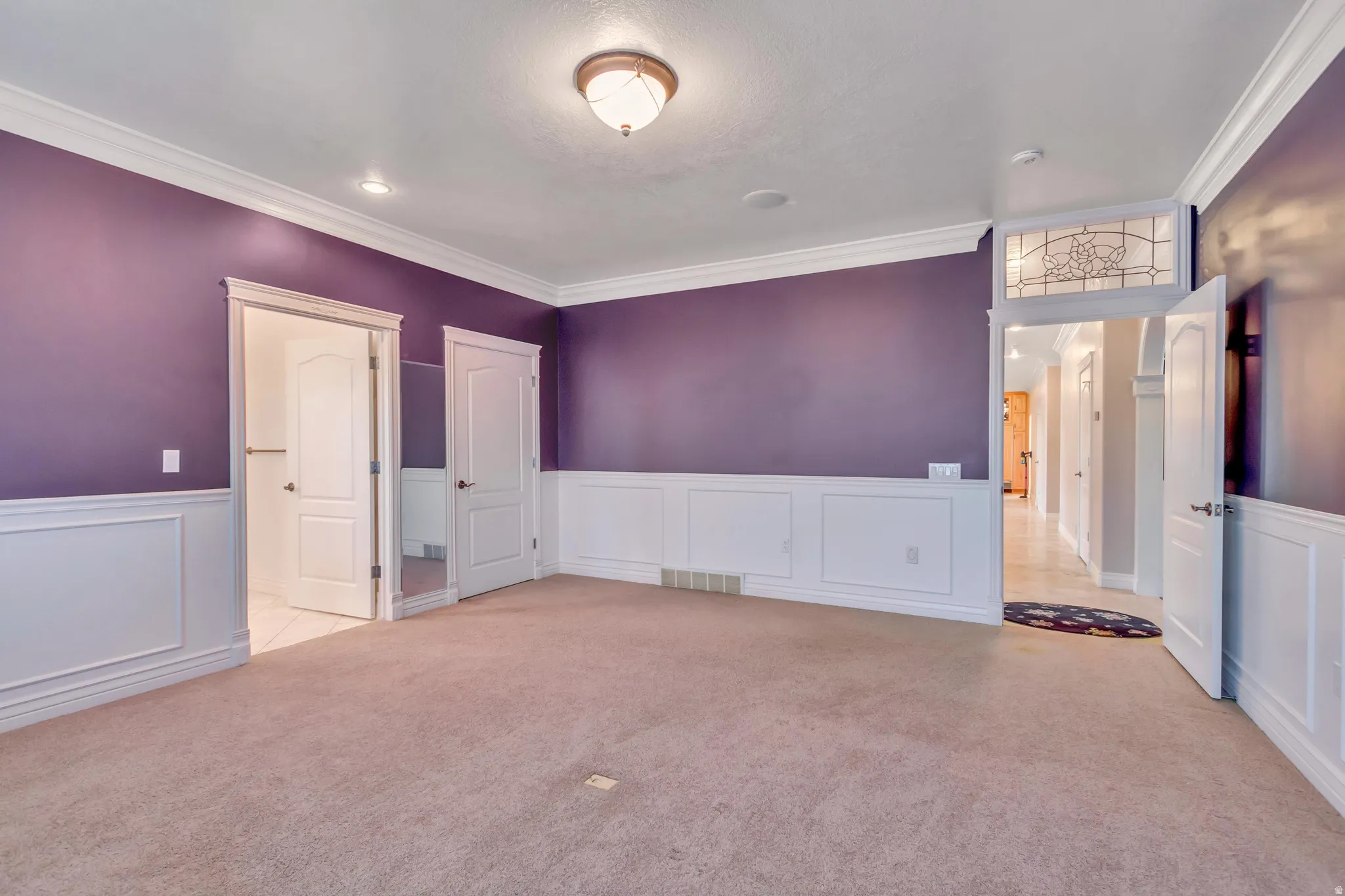 Carpeted interior space featuring wainscoting, crown molding, and two panel doors