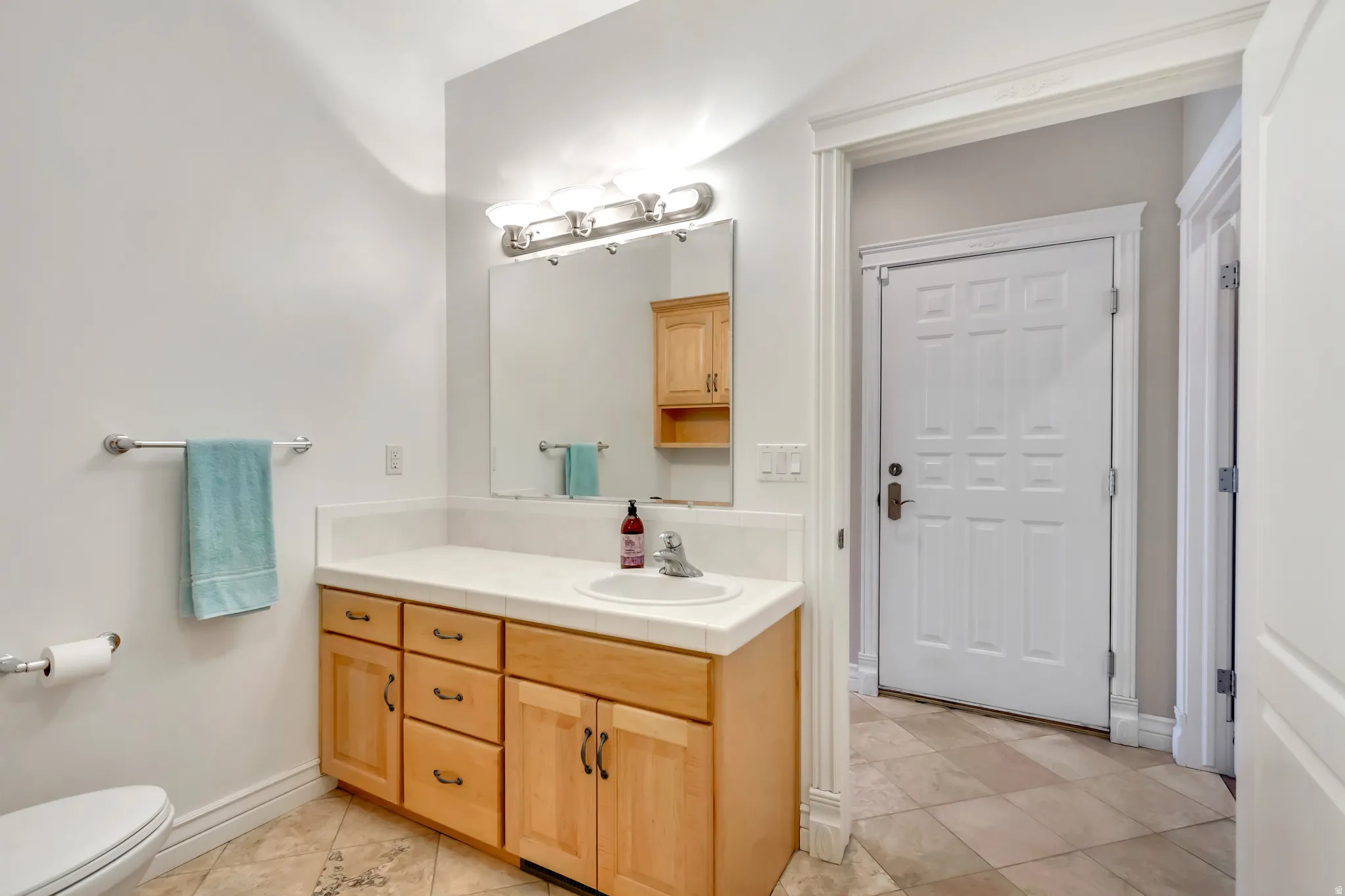 Light-toned wood vanity with a white countertop and integrated sink, complemented by a rectangular mirror and a four-bulb vanity light