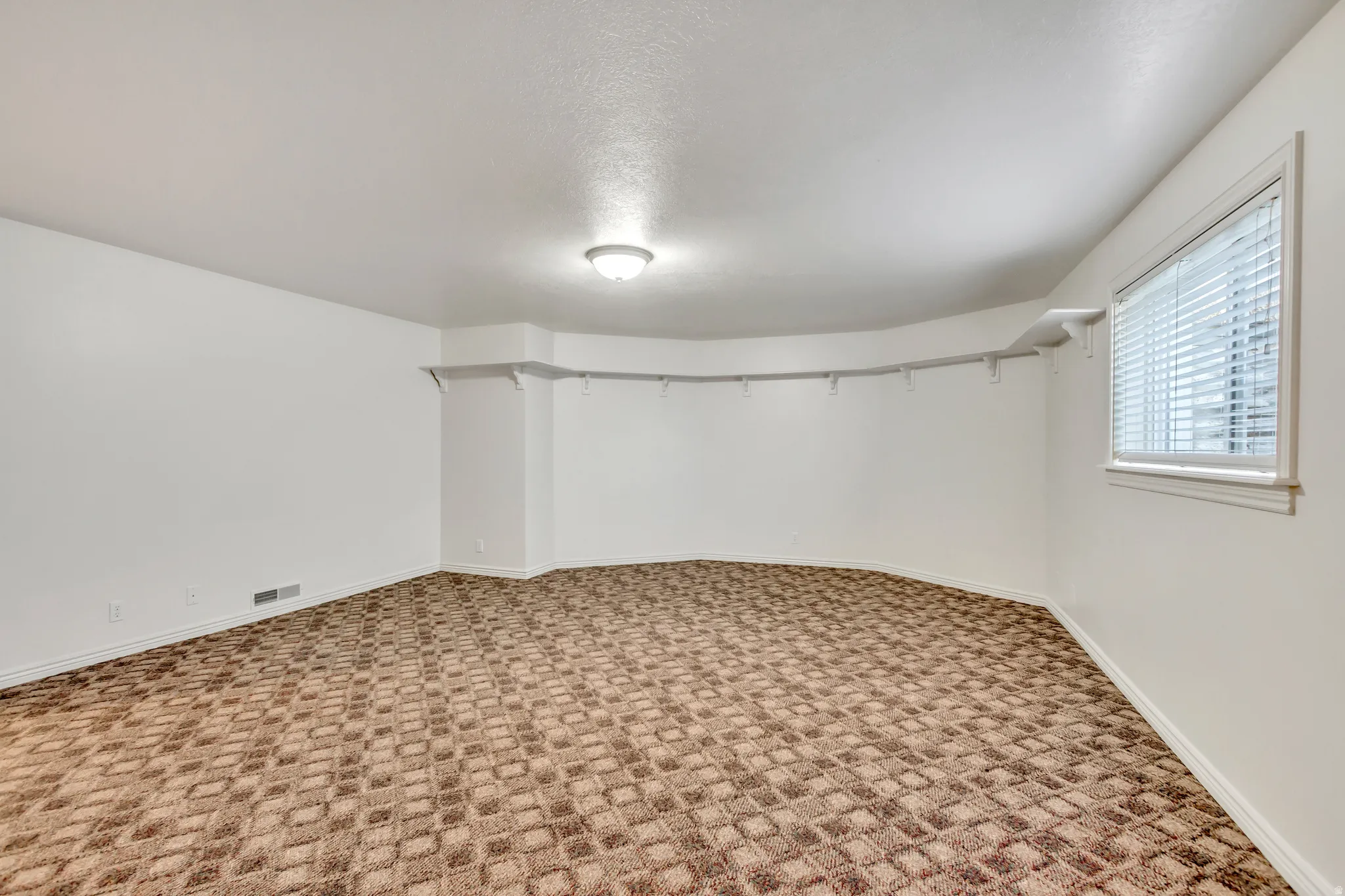 Spacious room featuring patterned carpeting, white painted walls, and a single window with blinds