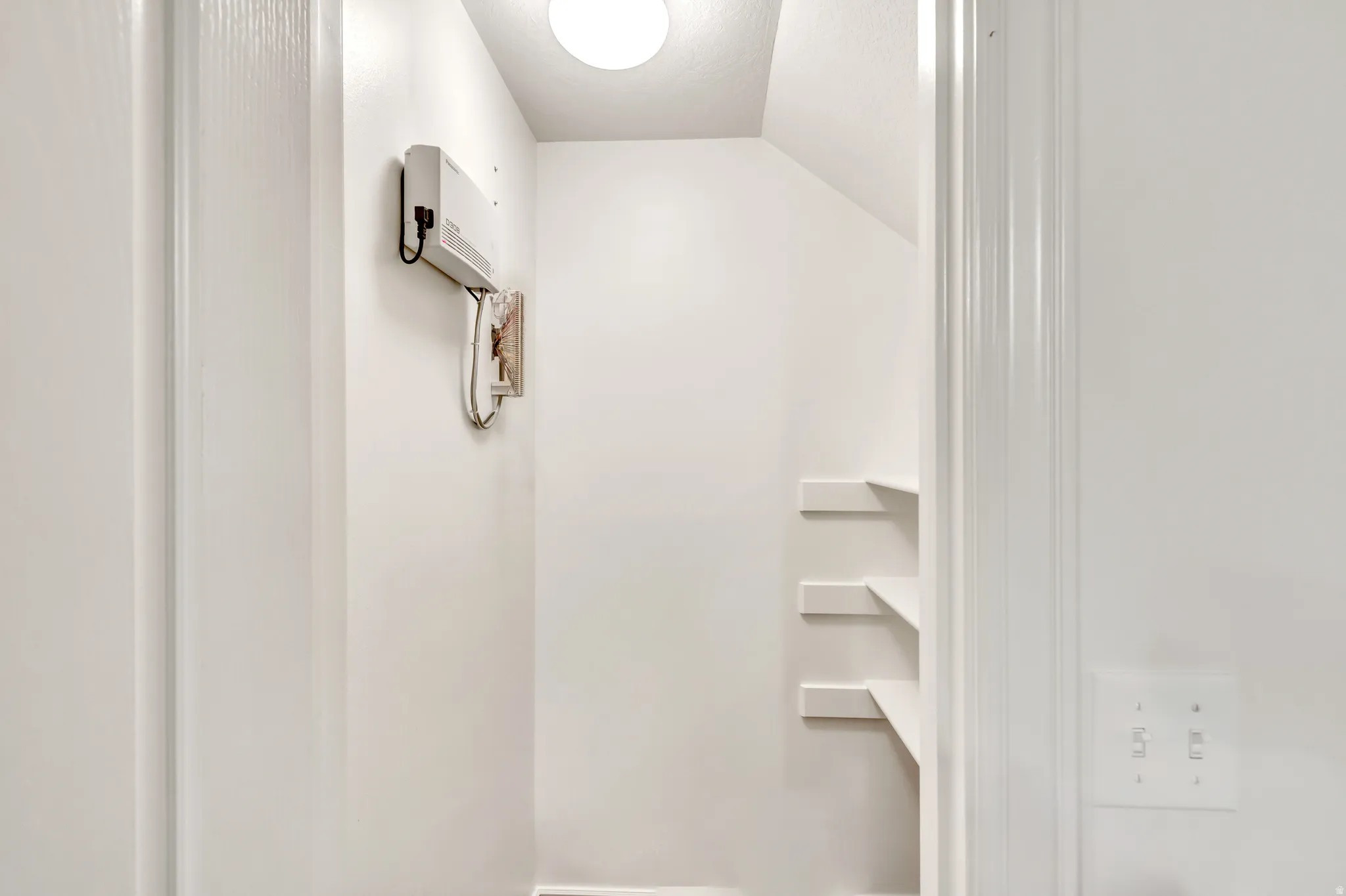 Under-stair storage area featuring multiple built-in shelves, white painted walls, and an overhead light fixture