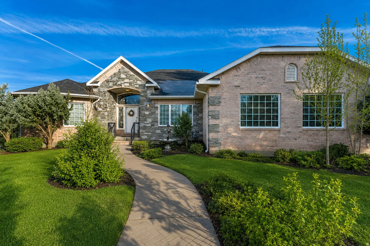 Stone and brick facade featuring a covered entry, arched transom window, and a winding paver walkway