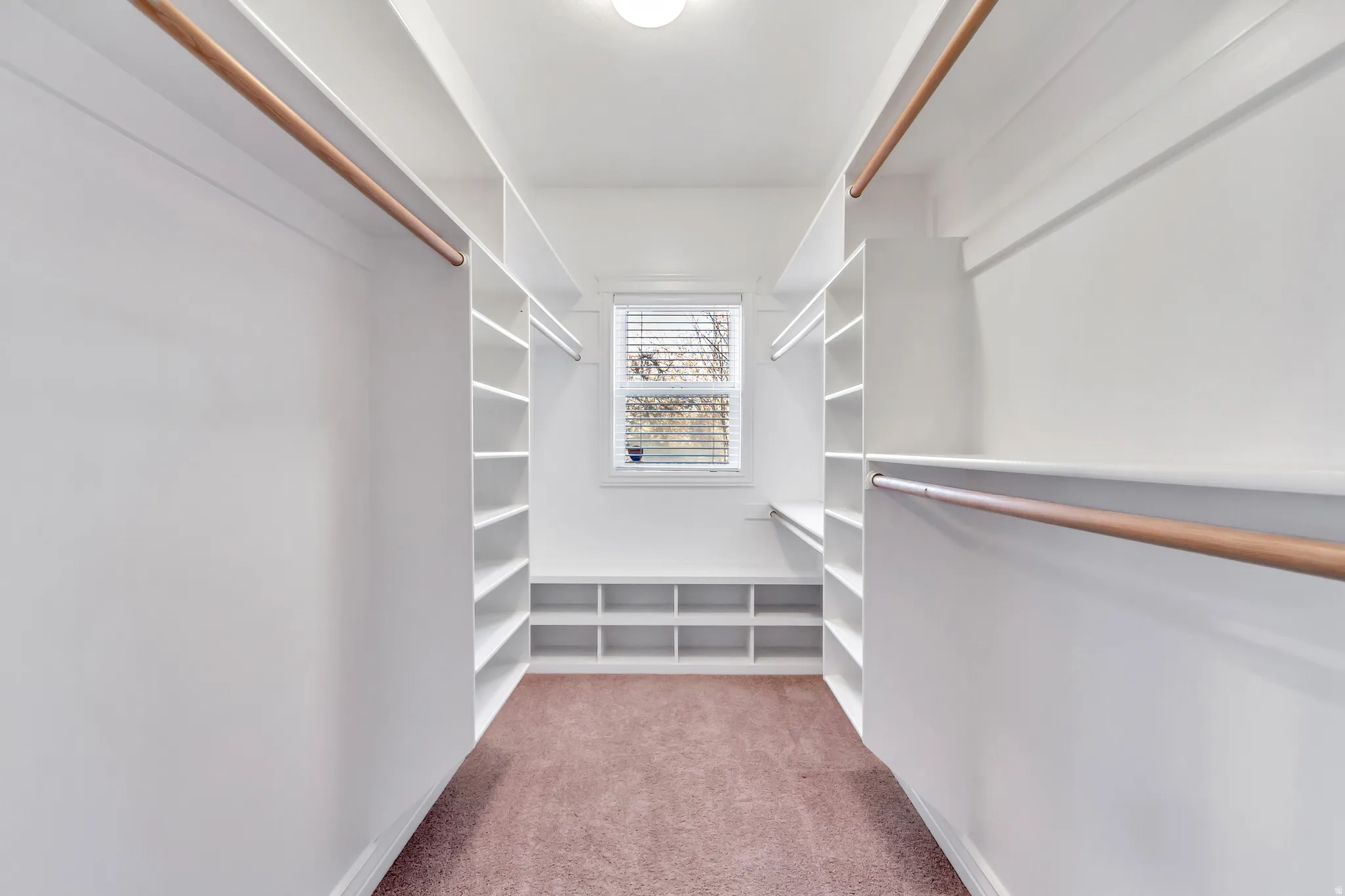 Walk-in closet featuring extensive built-in shelving, multiple hanging rods, and a window with horizontal blinds