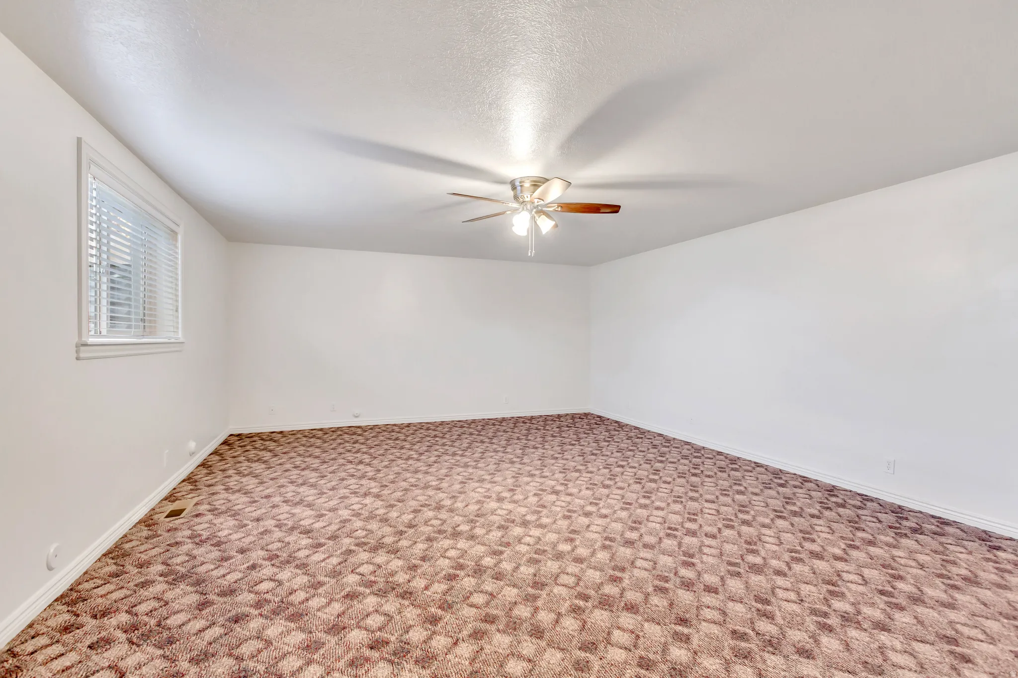 Carpeted room featuring a ceiling fan with integrated lighting, white walls, and a window with blinds
