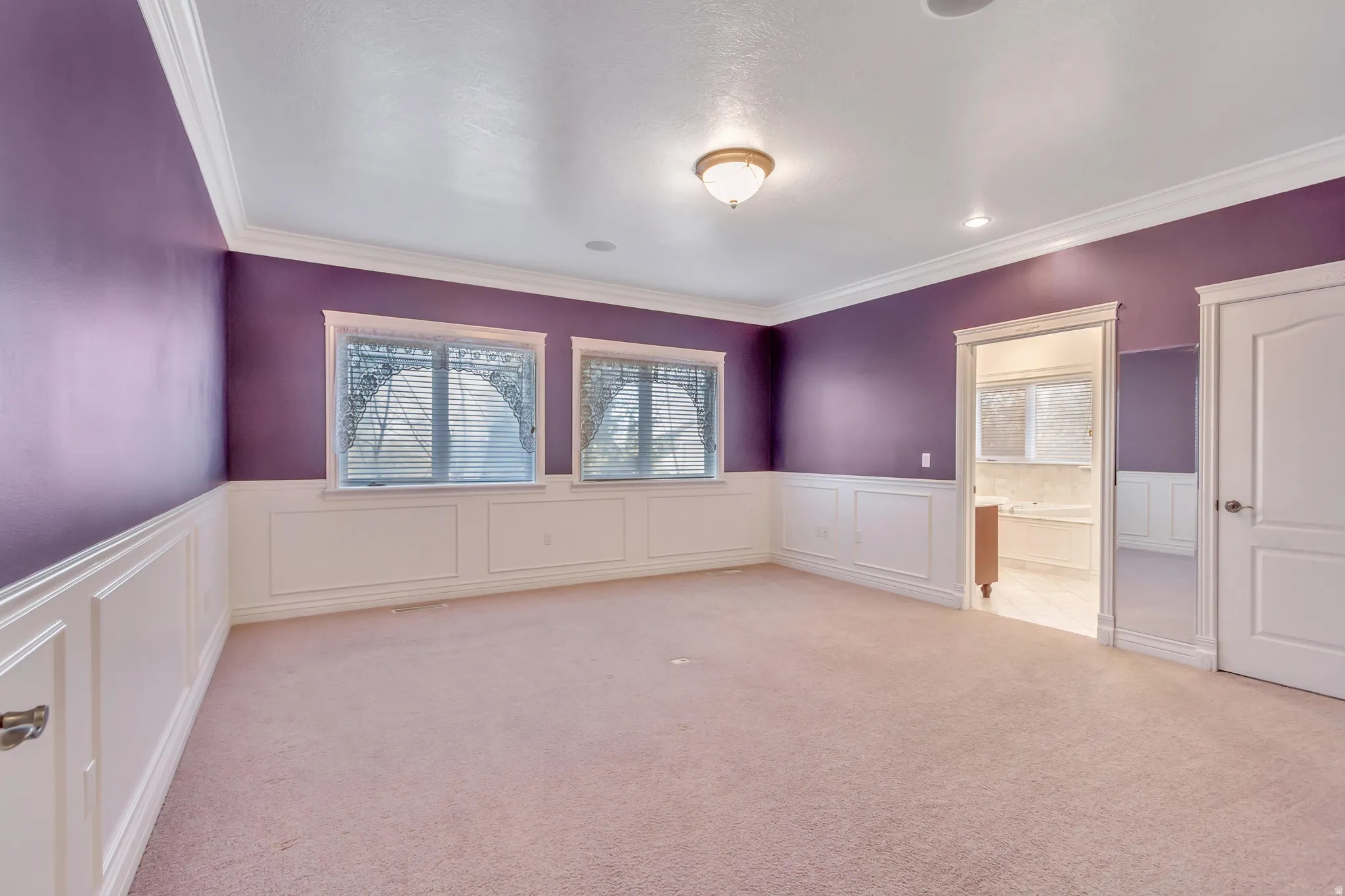Spacious room featuring two windows with blinds, wall paneling, crown molding, and recessed lighting