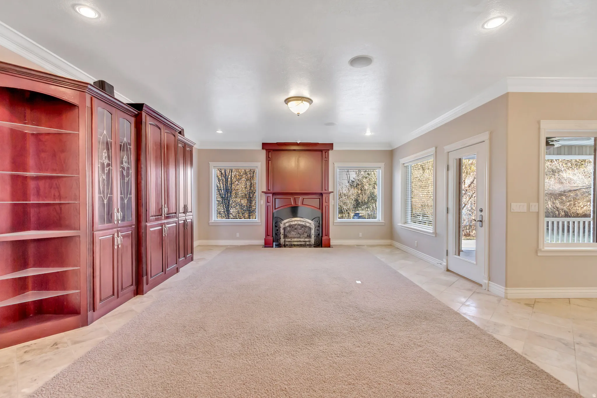 Spacious living area featuring extensive built-in mahogany cabinetry, a central fireplace with an ornate mantel, recessed lighting, and multiple windows