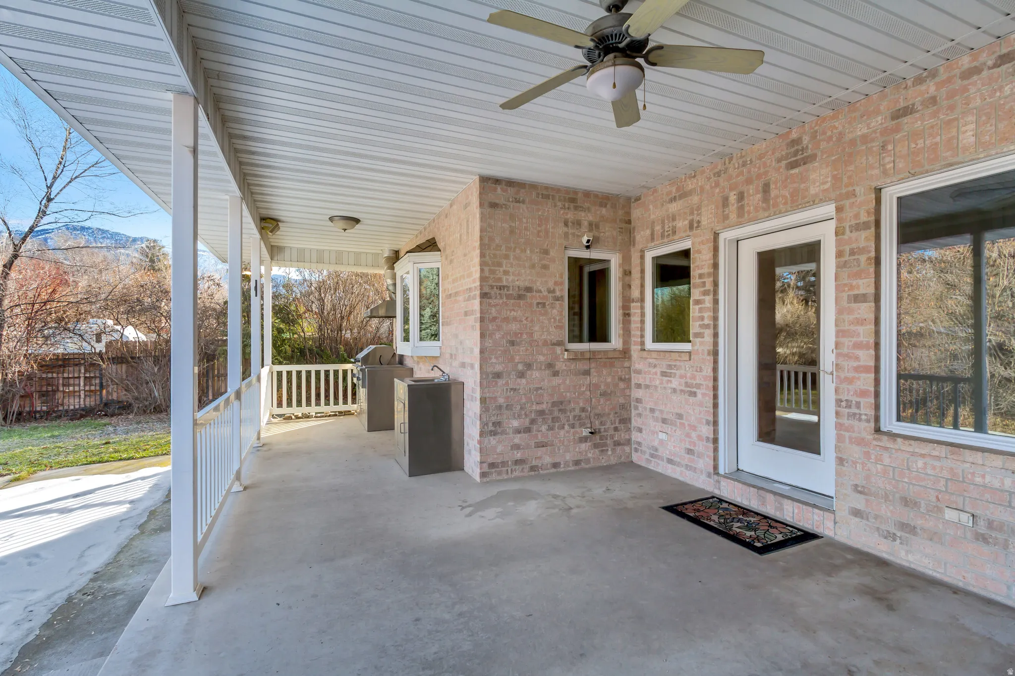 Spacious covered patio featuring brick exterior, white railing, concrete flooring, and multiple lighting fixtures